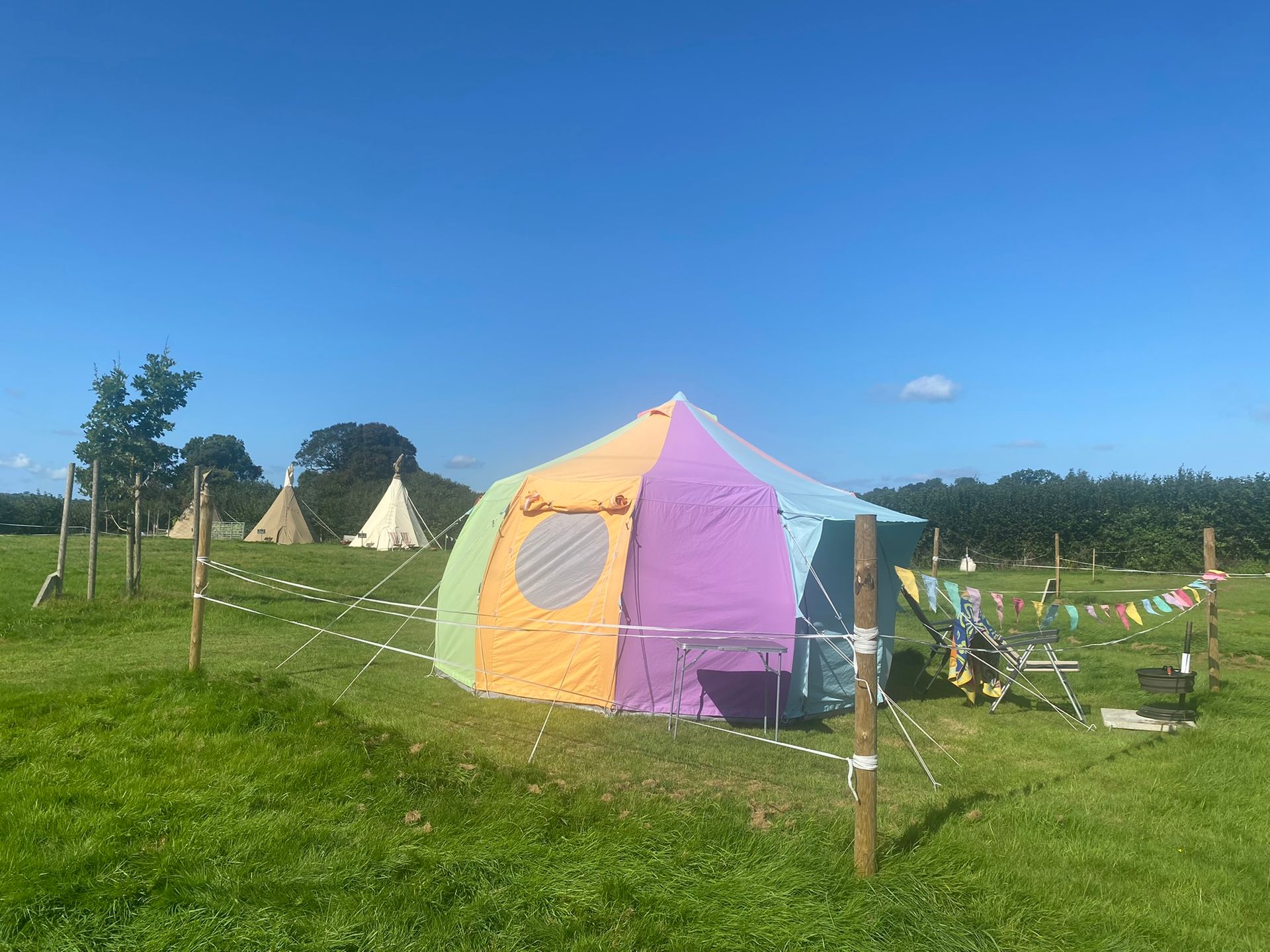 Colorful tent in a grassy field under a clear blue sky, with bunting and small teepee tents nearby