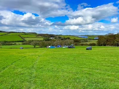 Bright green countryside field under a partly cloudy blue sky, with rolling hills in the distance.