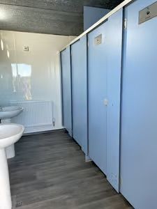 Row of light blue restroom stalls beside white sinks and a radiator on a dark floor