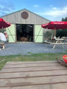 Outdoor barn-style café with red umbrellas, picnic tables, and open double doors on a gravel patio.