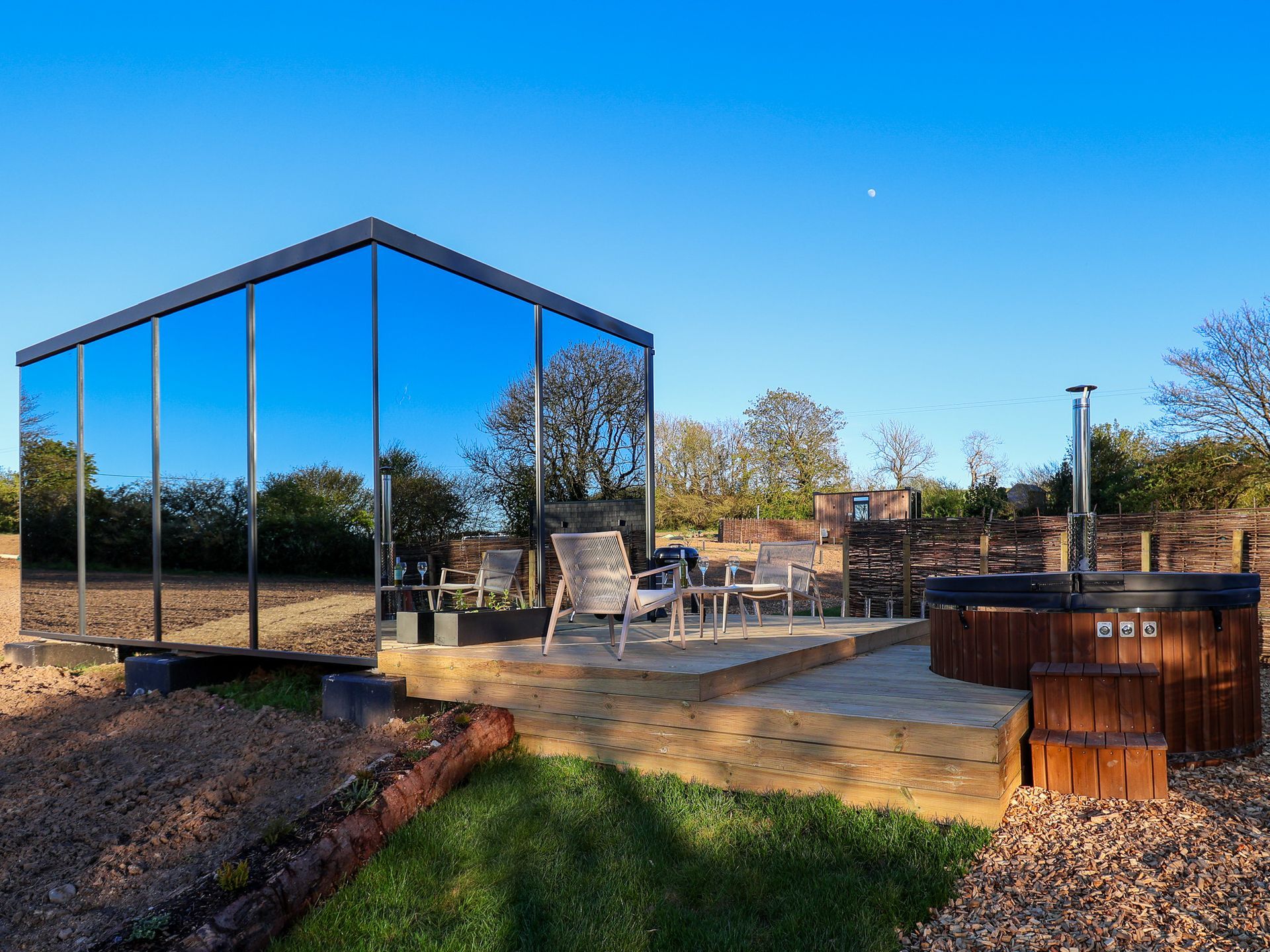 Mirrored tiny house with a patio, outdoor seating, and fire pit in a sunny yard