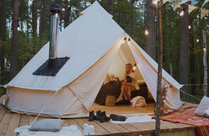 Canvas glamping tent on a wooden deck in a pine forest, with boots and a lit interior visible