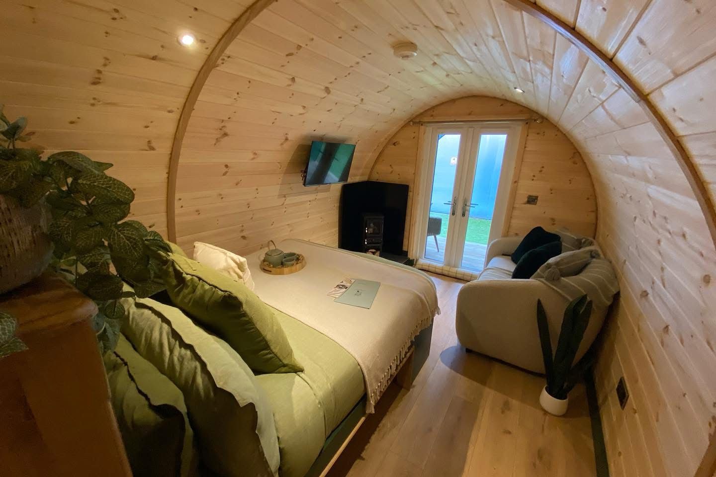 Cozy wooden cabin bedroom with a bed, sofa chair, and arched window