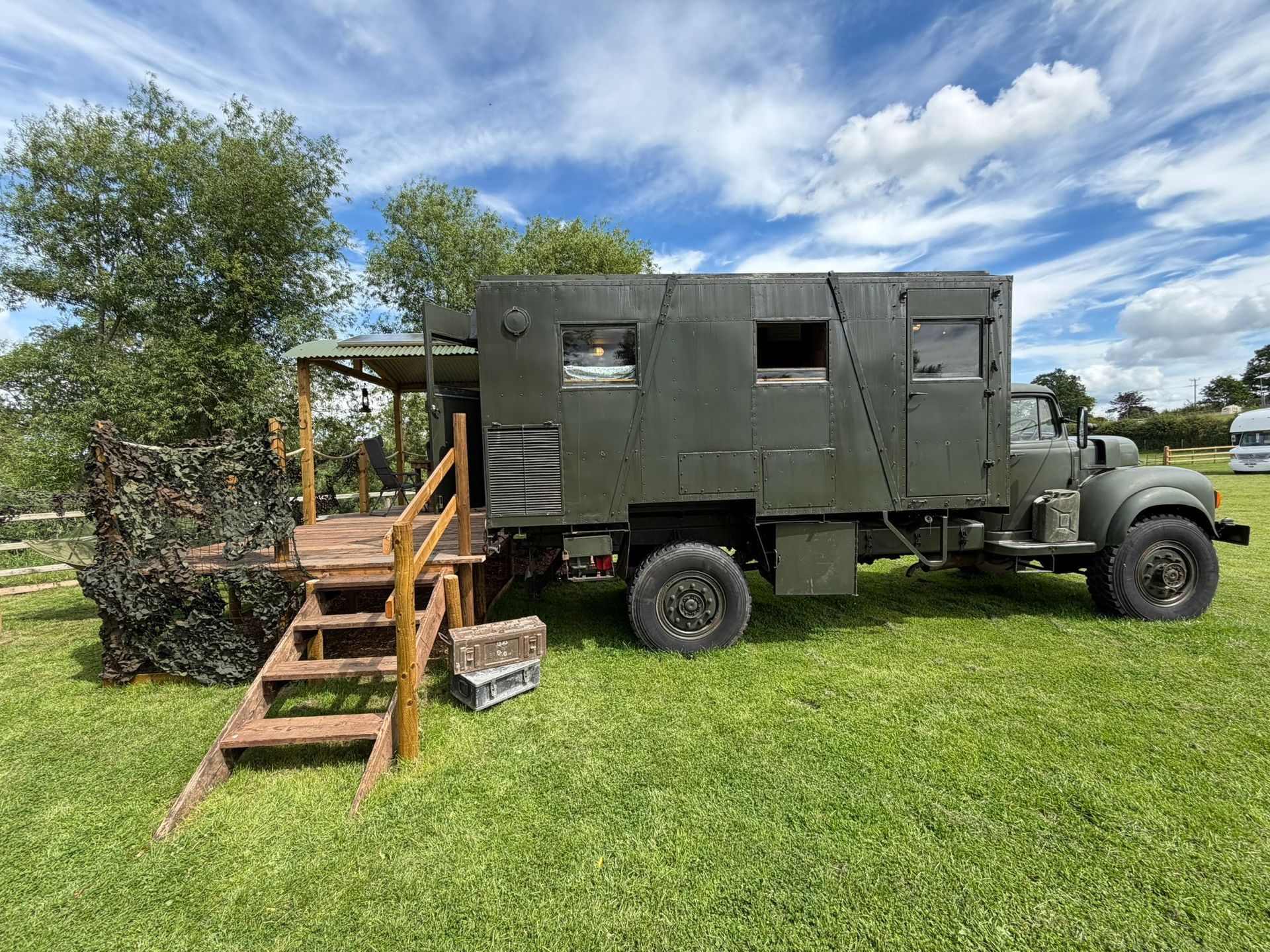 Olive-green military-style truck with a wooden ramp on grass under a blue sky