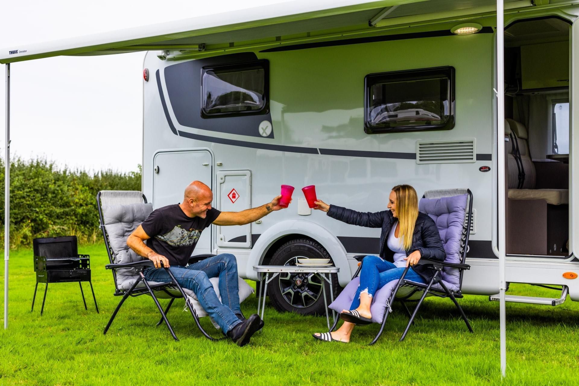 Two people relaxing in camping chairs outside a motorhome under a green awning