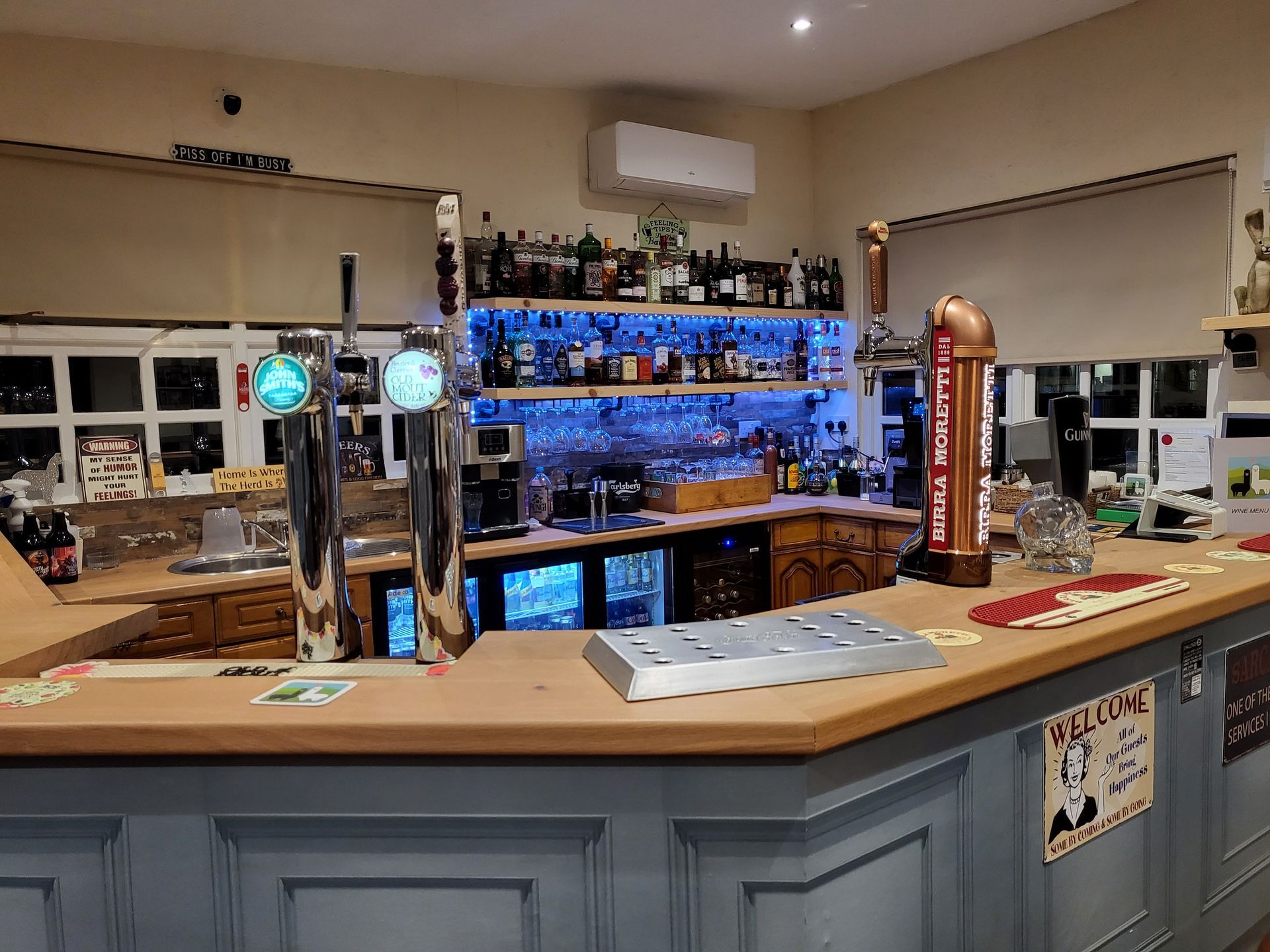 Bar with blue-lit shelves, beer taps, and bottles behind a wooden counter in a cozy pub.