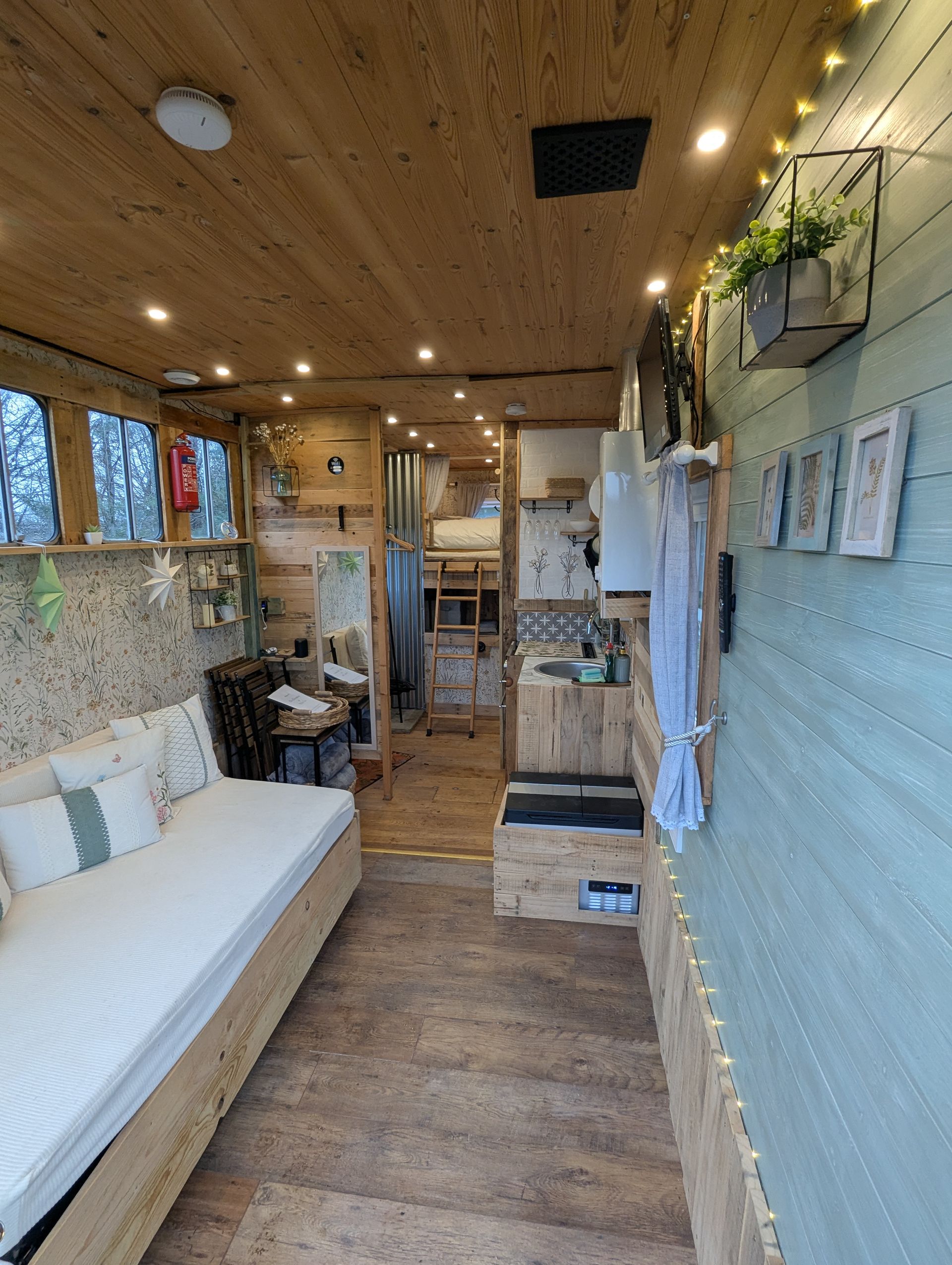 Narrow cozy cabin interior with white sofa, wood ceiling, small kitchenette, and shelves along the wall