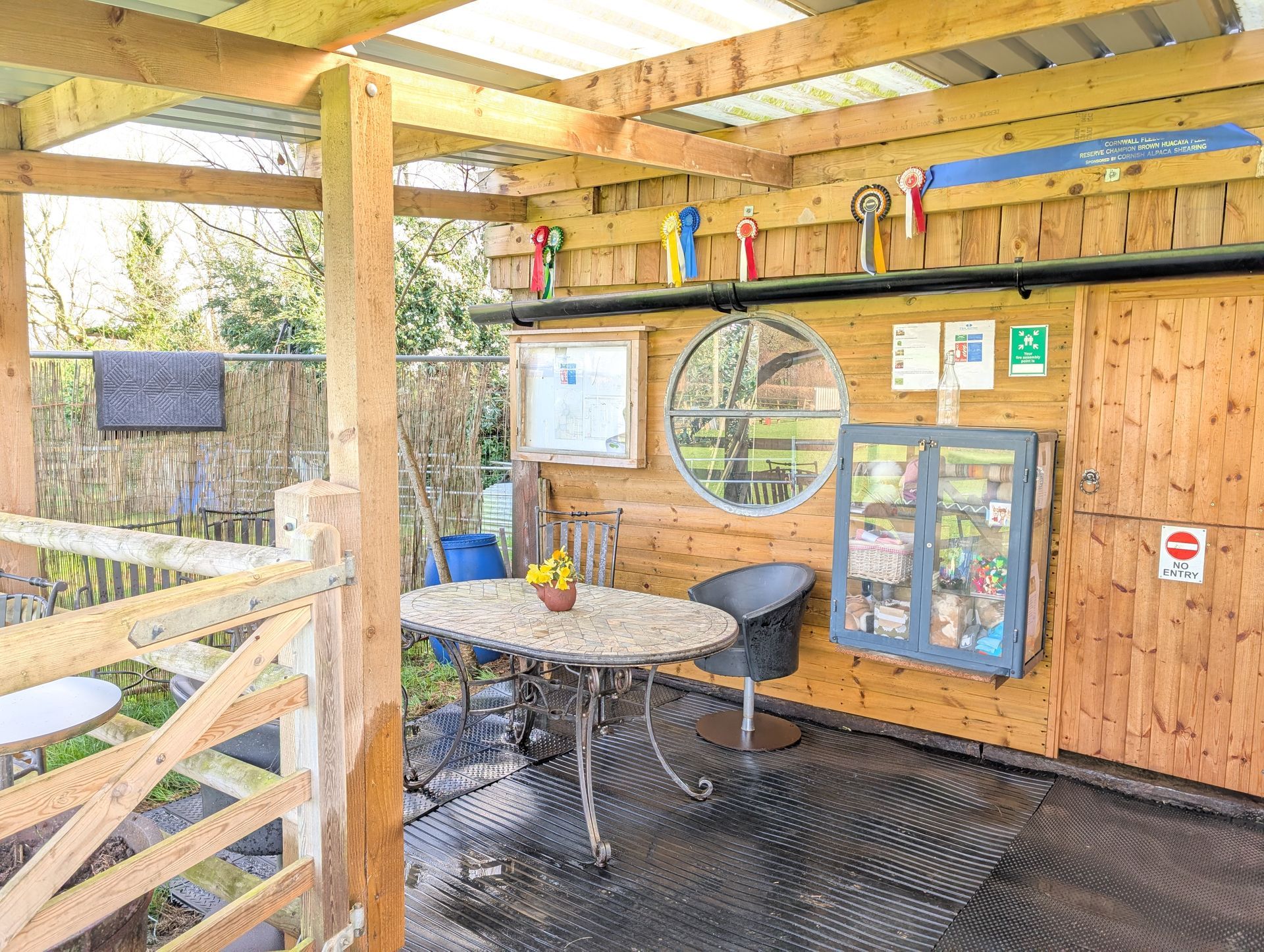 Wooden outdoor shelter with a round table, stools, shelves, and hanging tools on a wet floor
