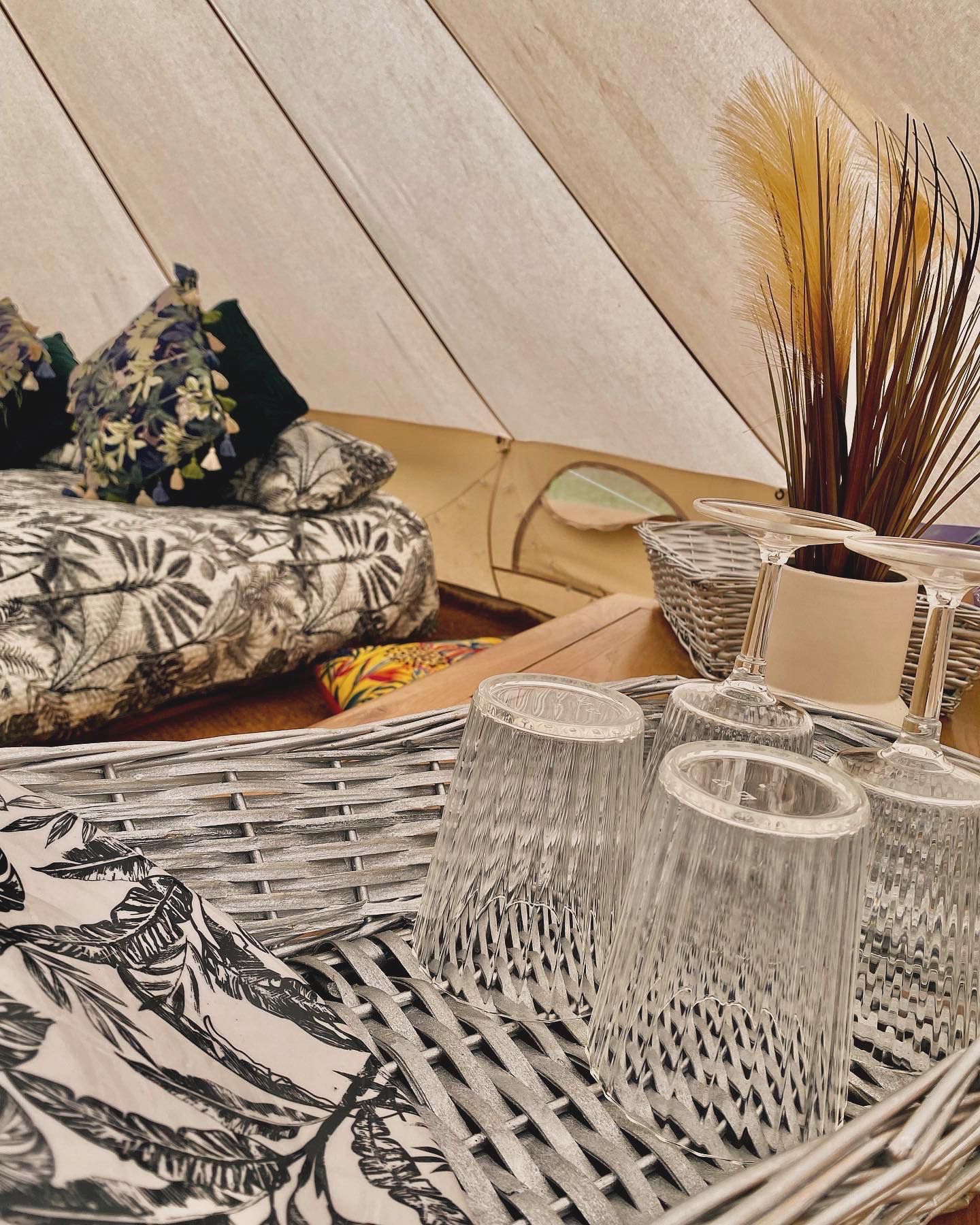 Cozy tent interior with patterned pillows, woven trays, and dried grasses on a light wood floor