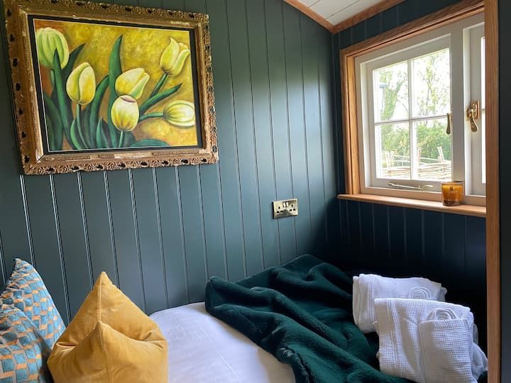 Cozy room with framed yellow flower painting, window light, and bed with pillows and folded towels