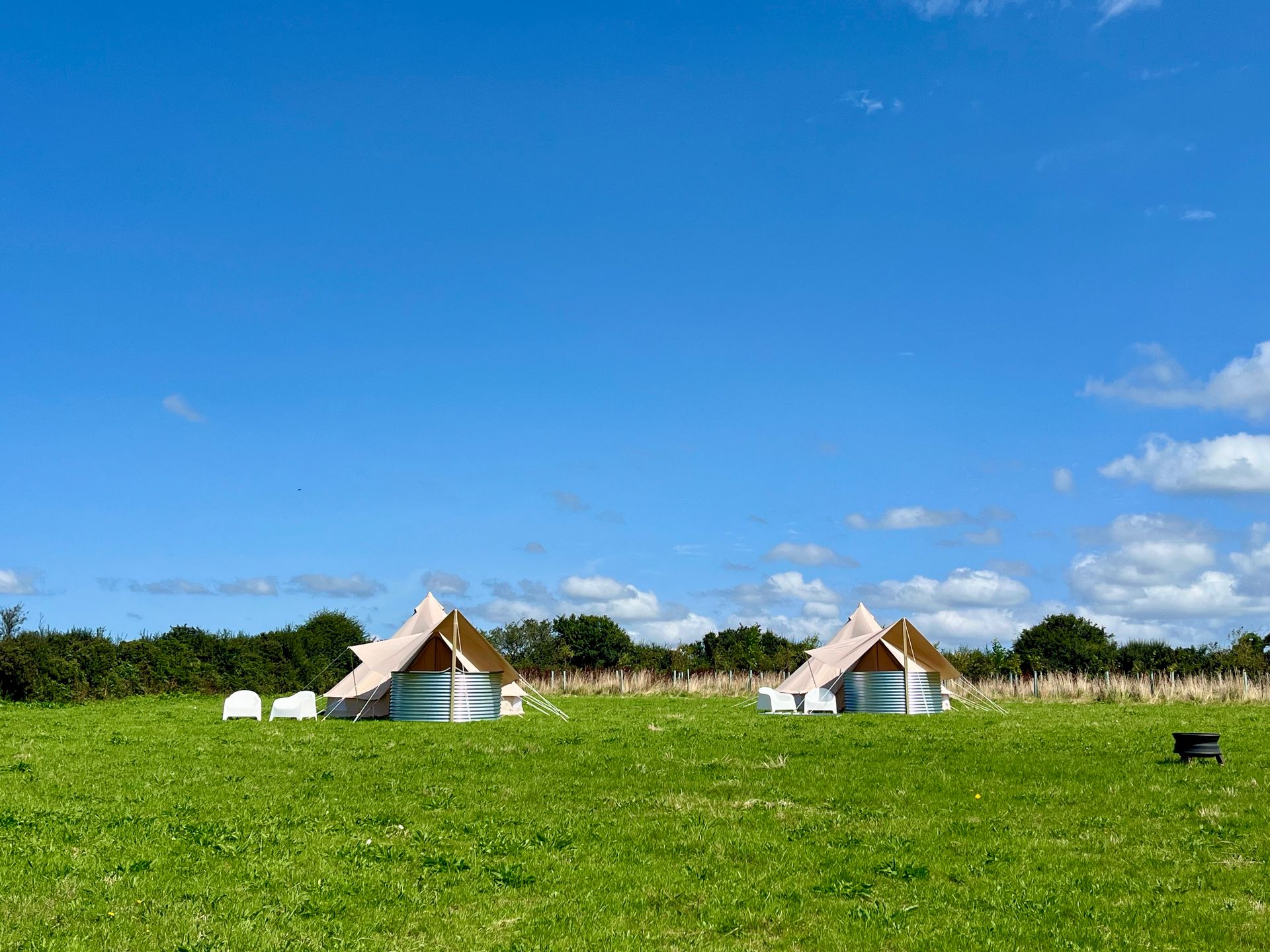Grassy field with two small white-roofed tents under a blue sky with scattered clouds