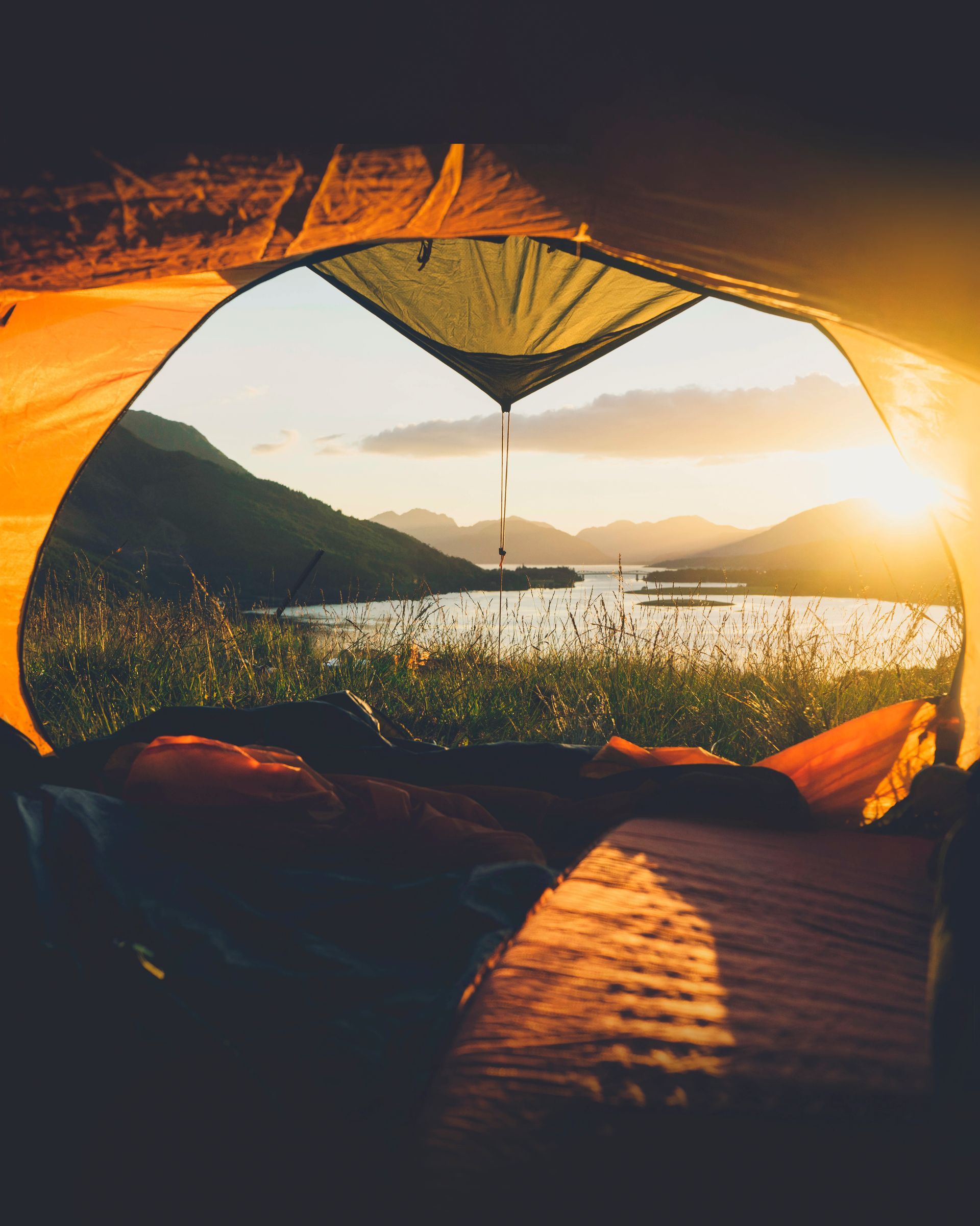 Sunrise view from inside a tent overlooking a lake, mountains, and glowing orange sky.
