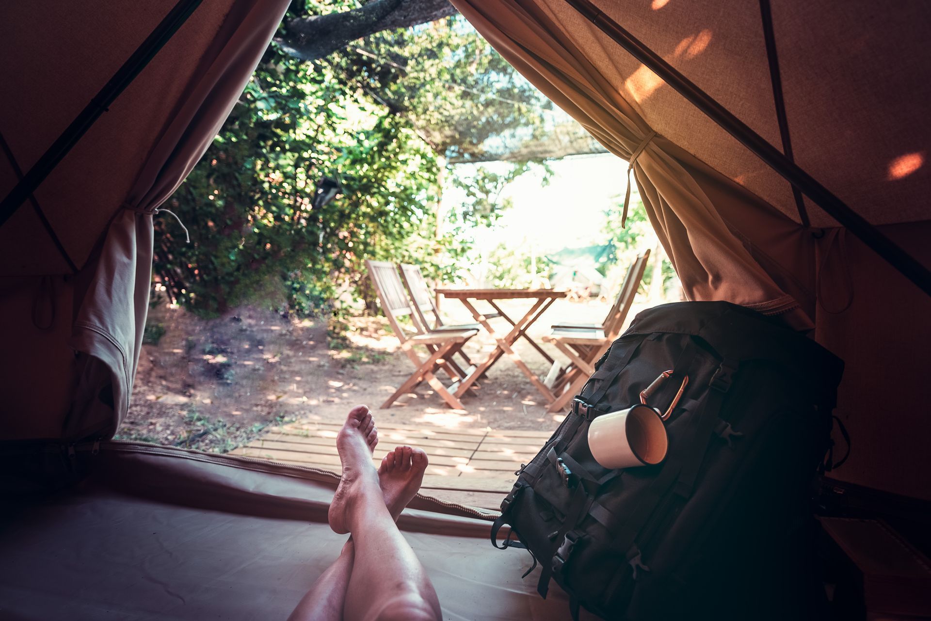 Inside a tent, feet up facing a sunlit campsite table and backpack at the entrance.