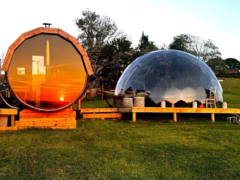Two dome-shaped structures on grass, one orange and one clear, at sunset.