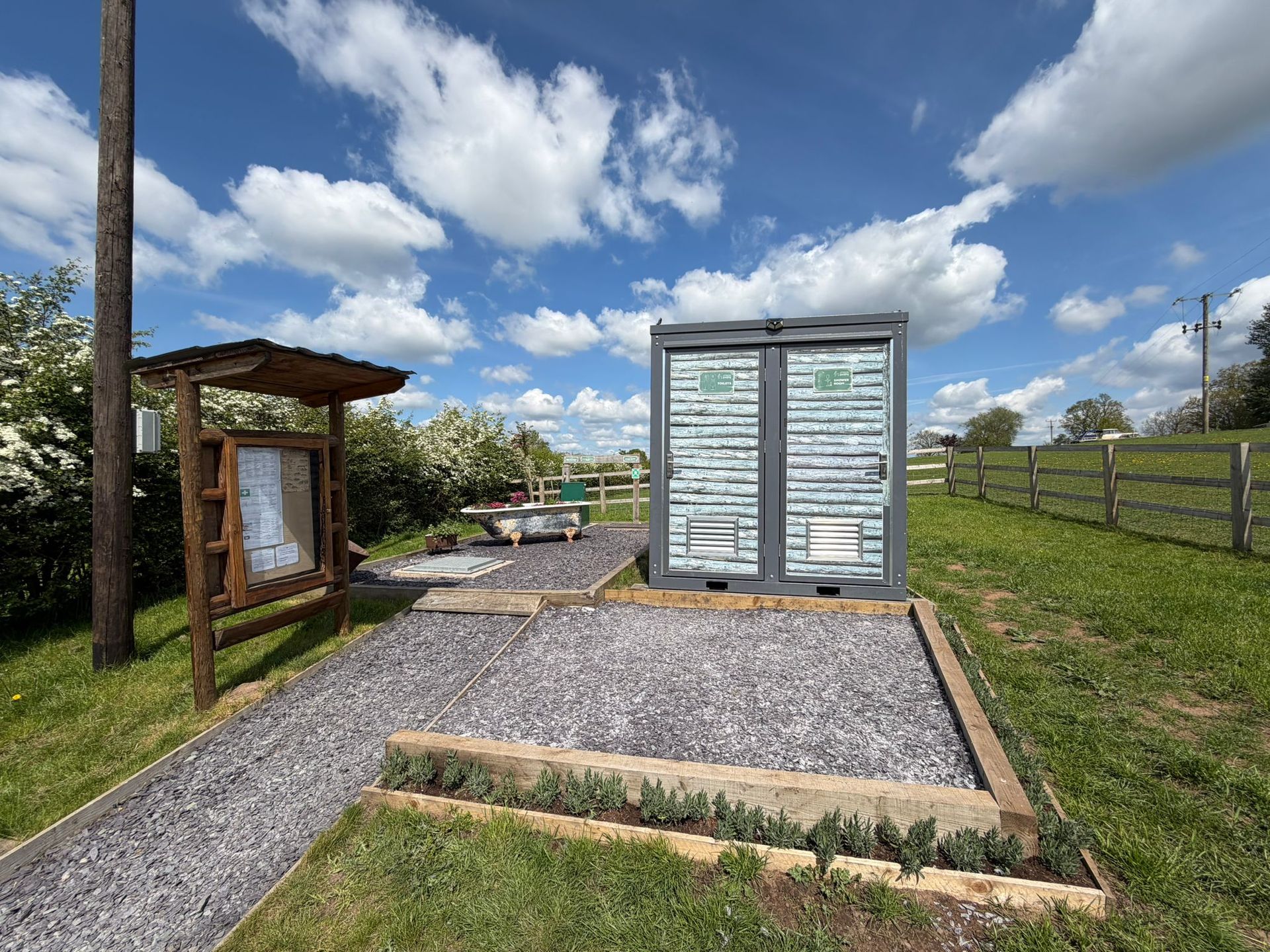 Gravel exhibit area with a small wooden shelter and a gray utility cabinet under a partly cloudy sky