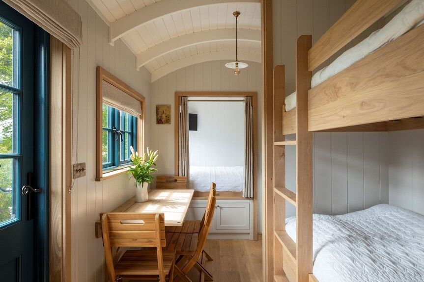 Narrow wooden hallway with bunk beds, a small desk, and window, lit by natural light