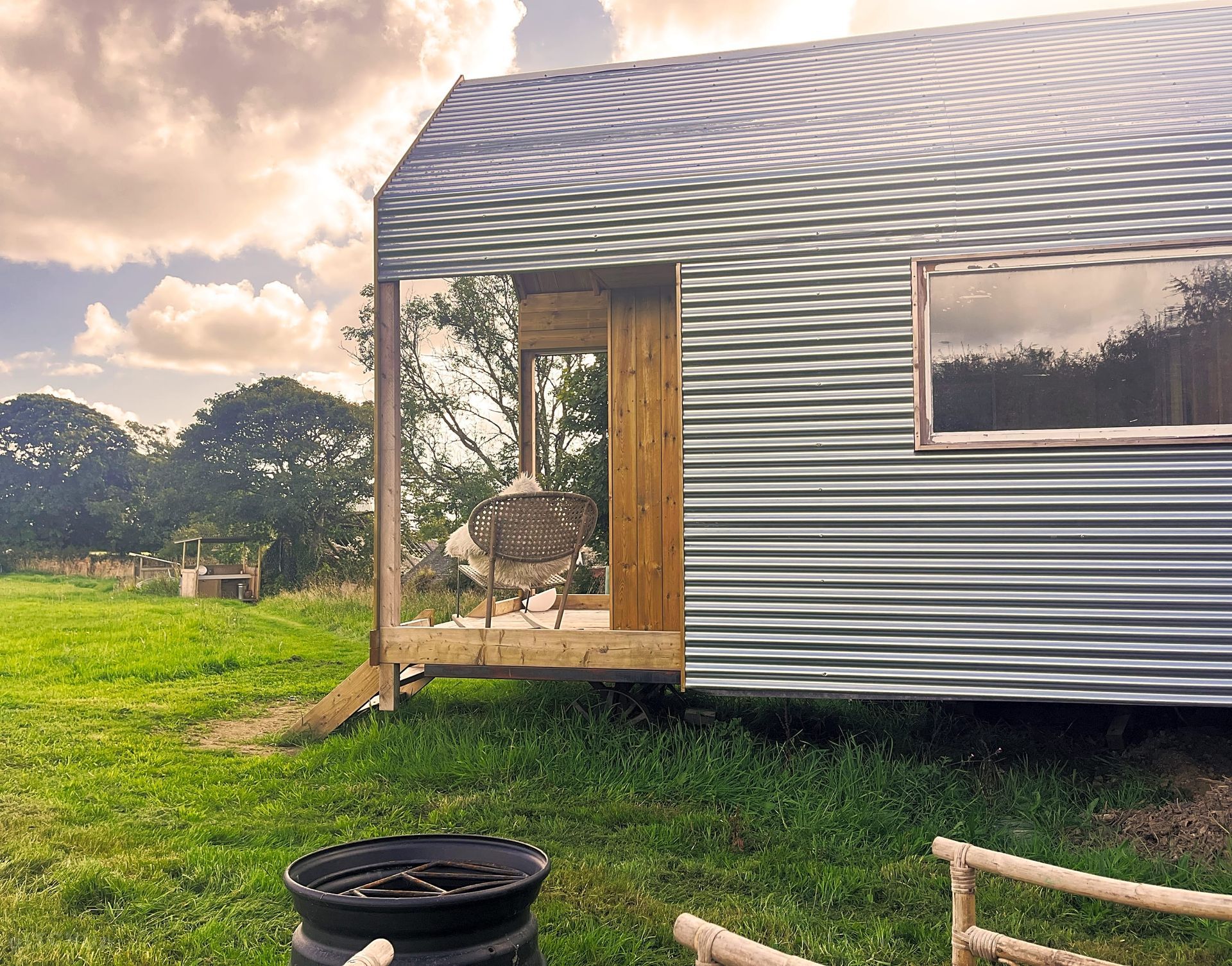 Silver-sided tiny house with open wooden doorway in a grassy field at sunset