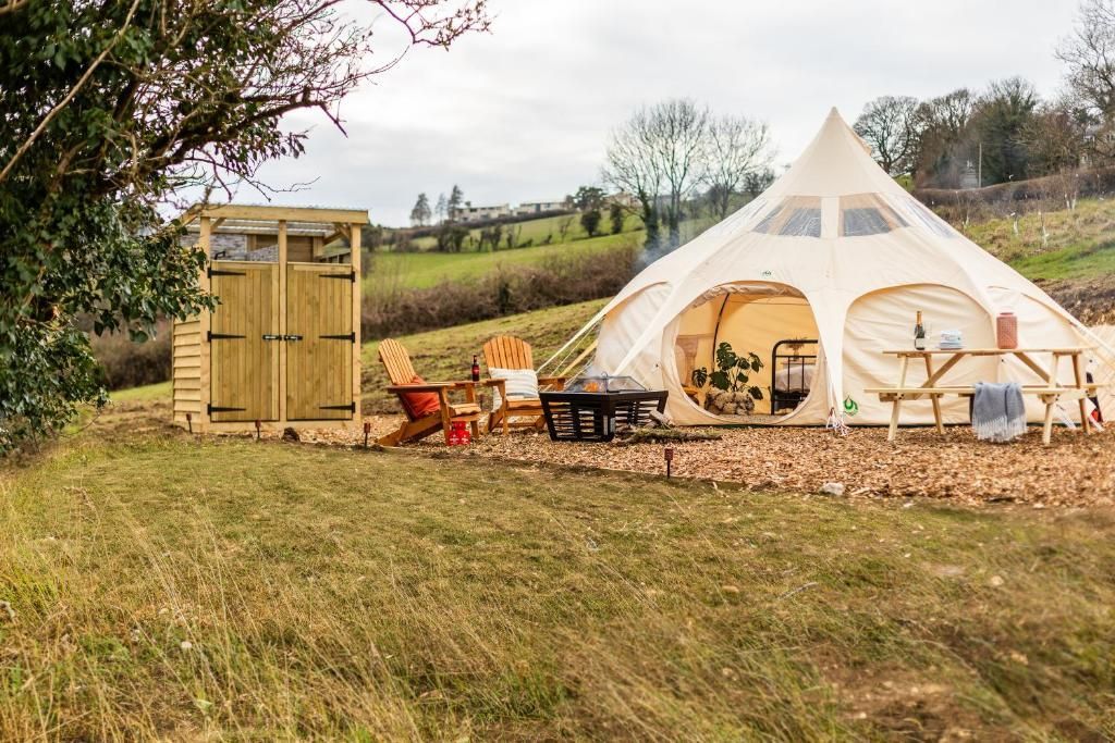 White tipi tent and wooden shed on a grassy field with chairs and a fire pit under a cloudy sky