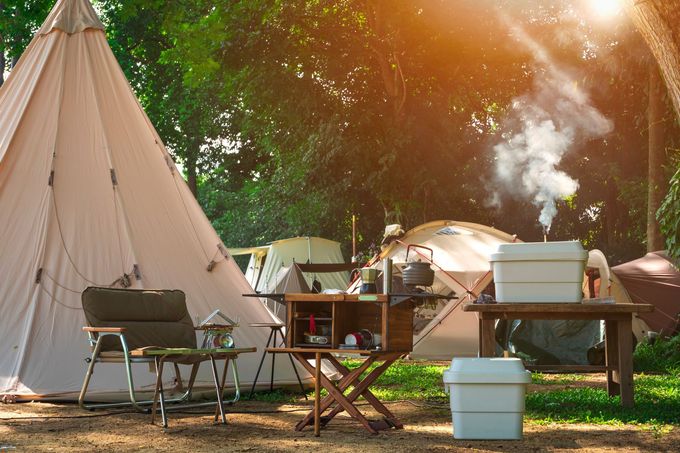 Campsite with a beige tent, folding chairs, picnic tables, and a kettle smoking in warm sunlight