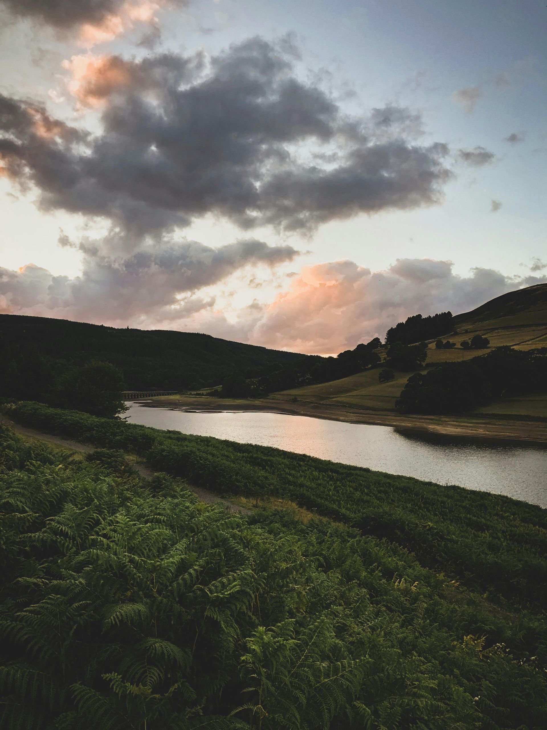 Cloudy sunset over a river with grassy banks and dark hills
