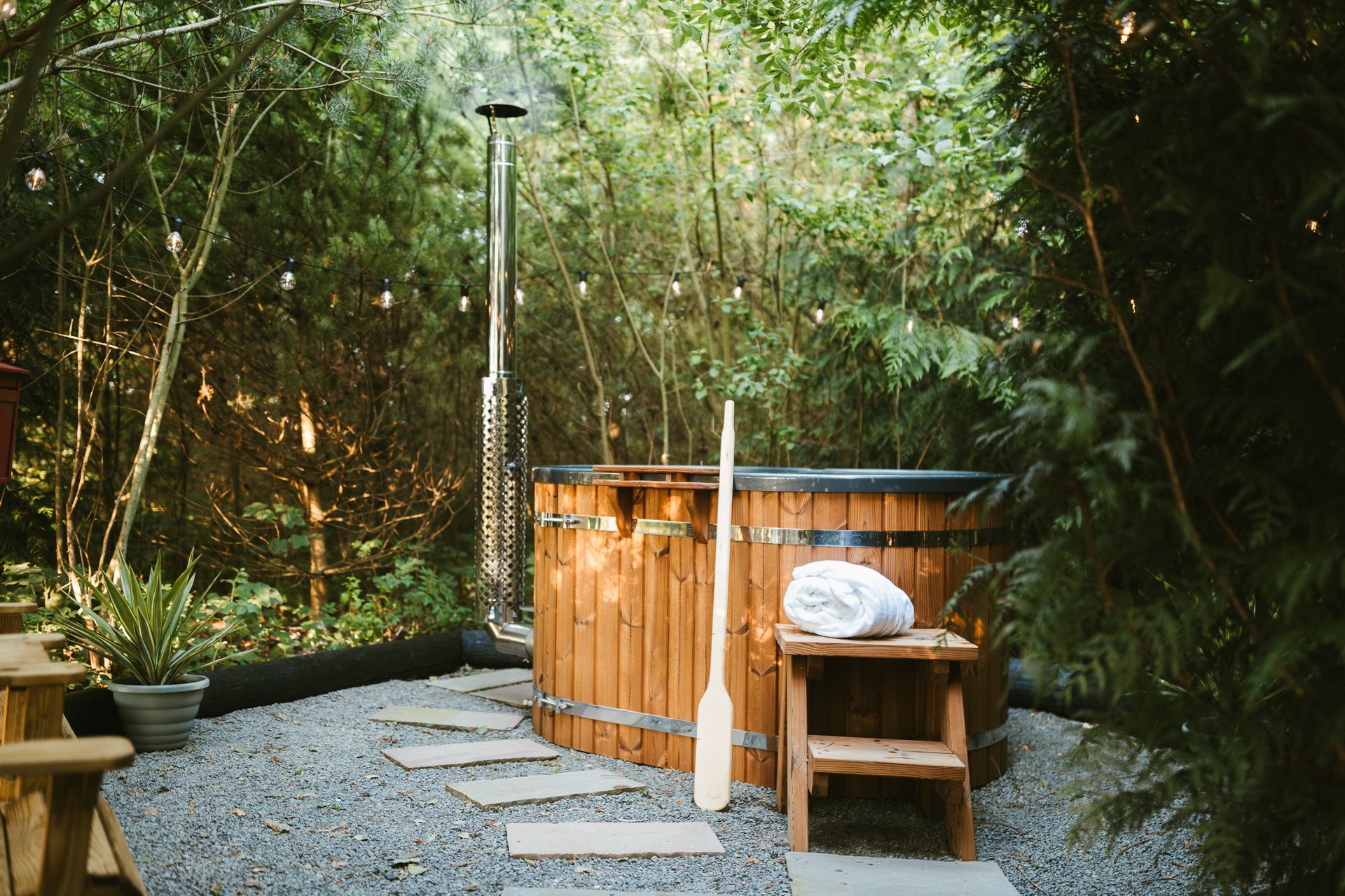 Outdoor wooden hot tub and chair on a gravel patio surrounded by lush bamboo greenery