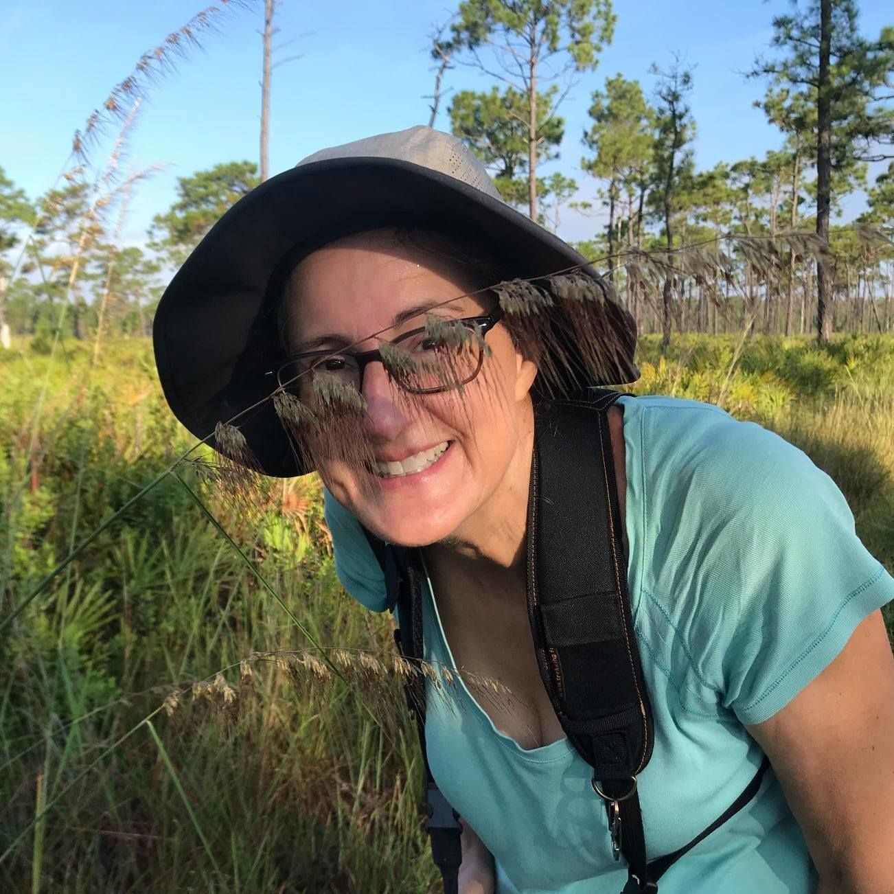 Laura Bennett-Kimble leaning down behind a flowering stalk of Lopsided Indiangrass