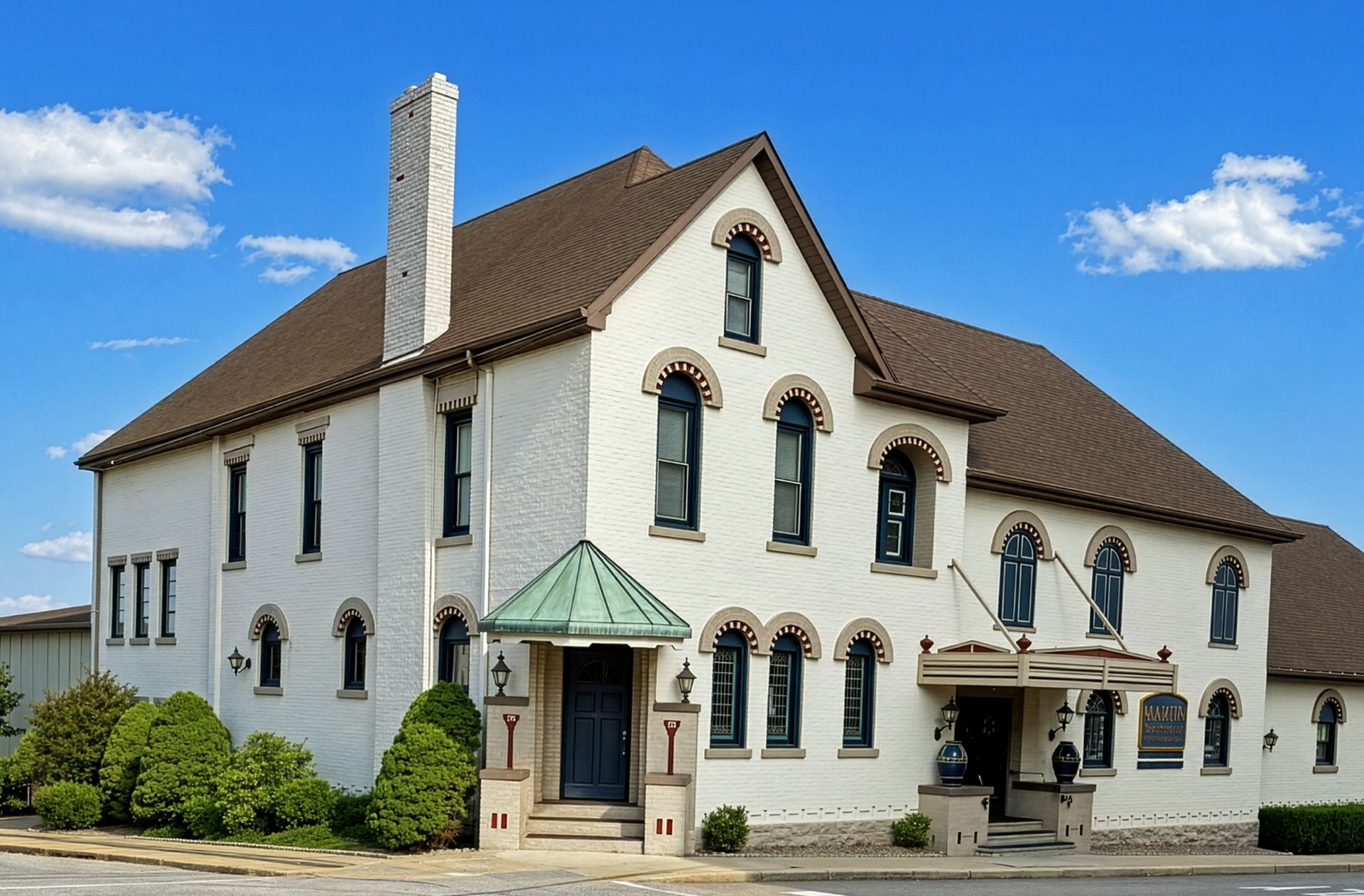 White historic building with red roof, arched windows, and a covered entrance under a blue sky