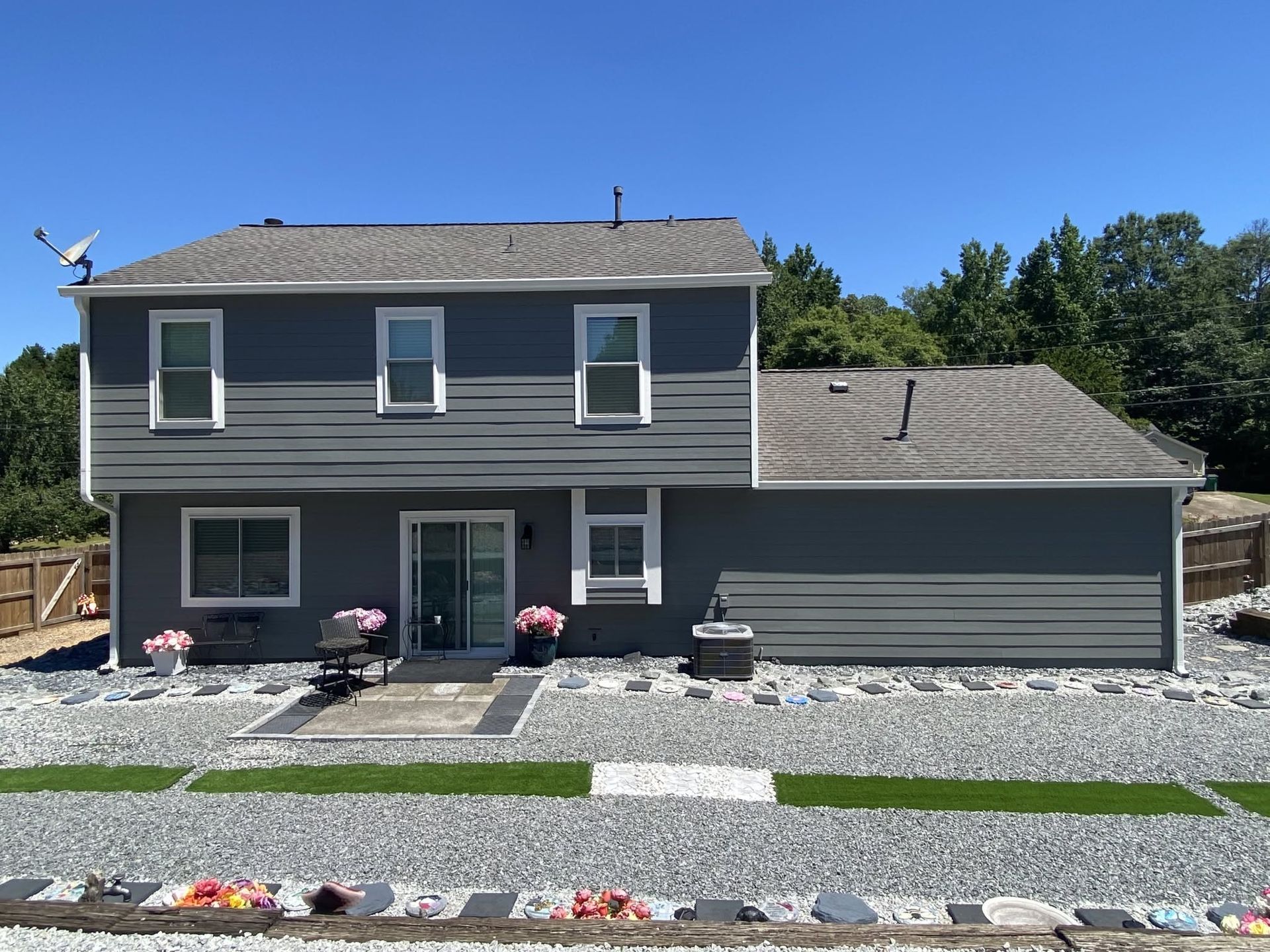 Gray two-story house with attached garage, stone landscaping, and red flowers under a blue sky
