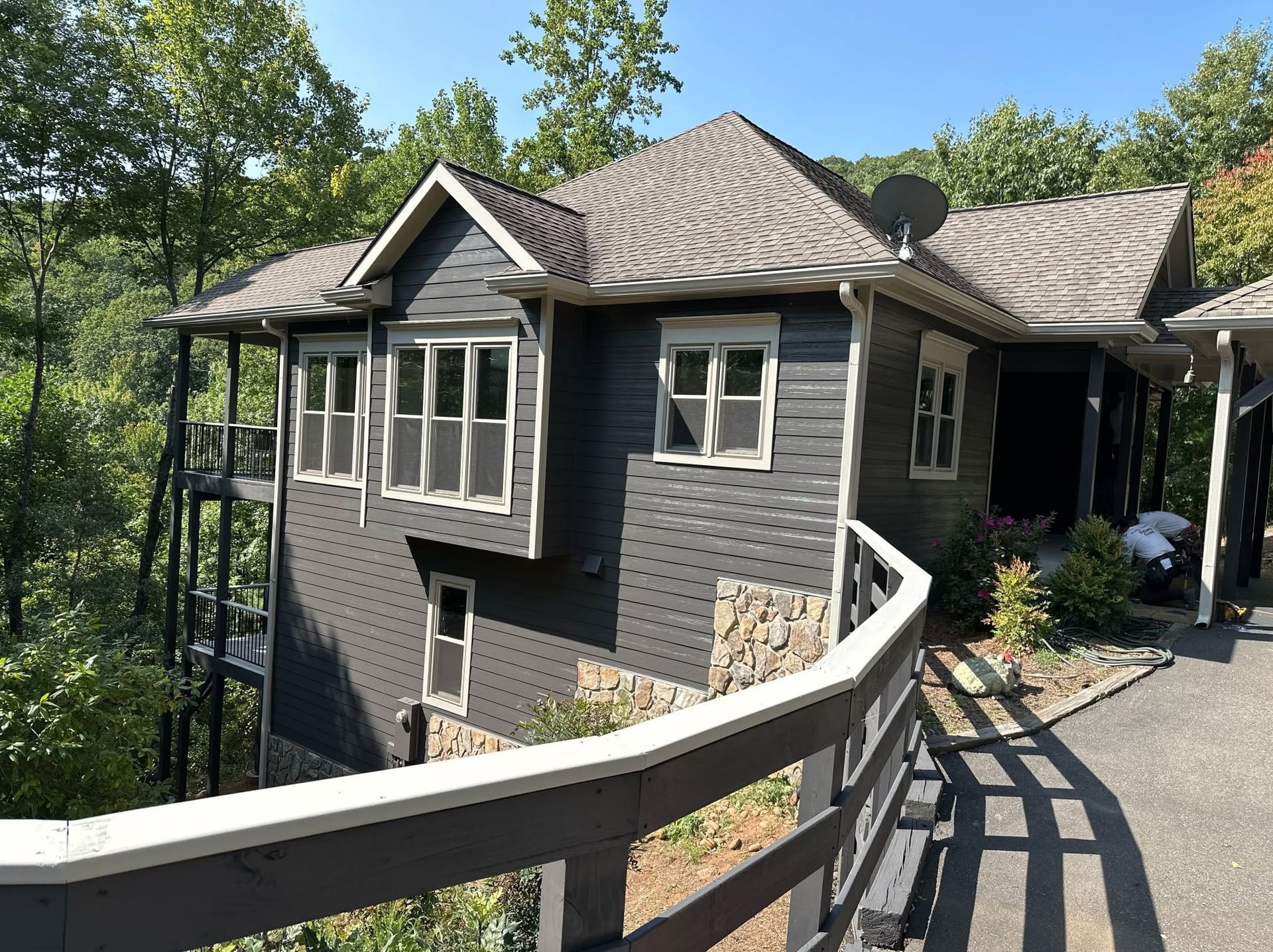 Curved walkway leading to a gray house with a shingled roof and trees in the background