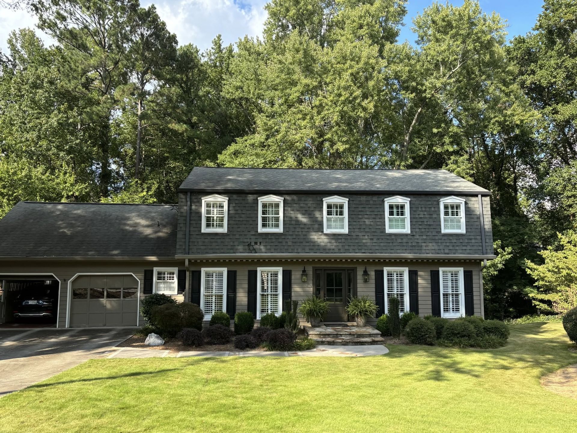 Two-story dark gray house with white trim and attached garage, surrounded by green lawn and trees