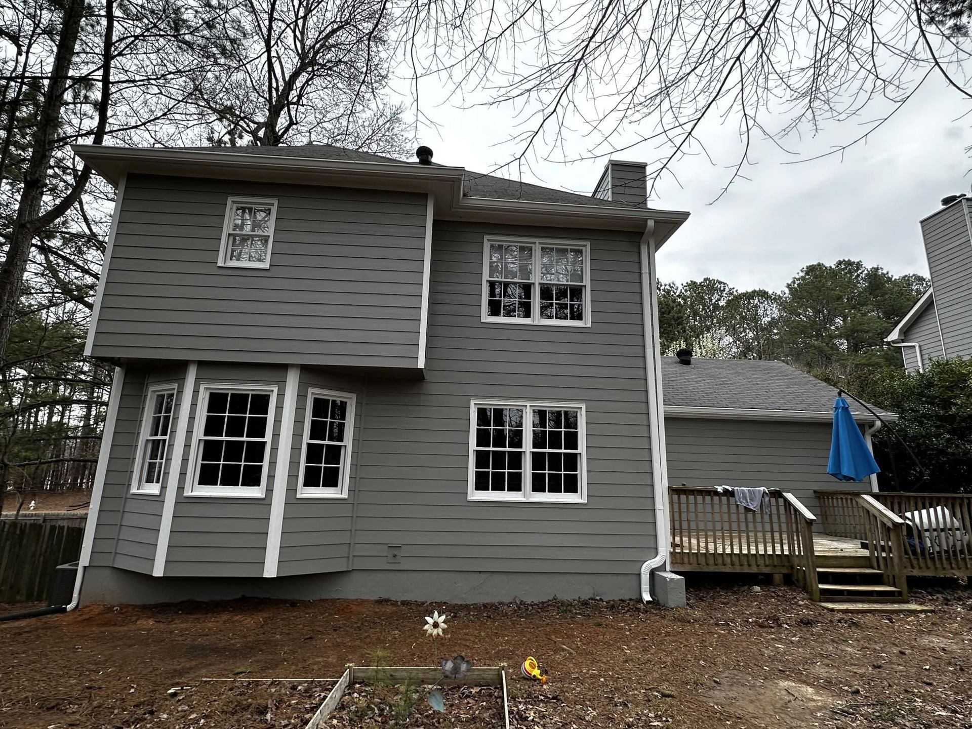 Gray two-story house with white-trim windows, backyard deck, and bare trees overhead