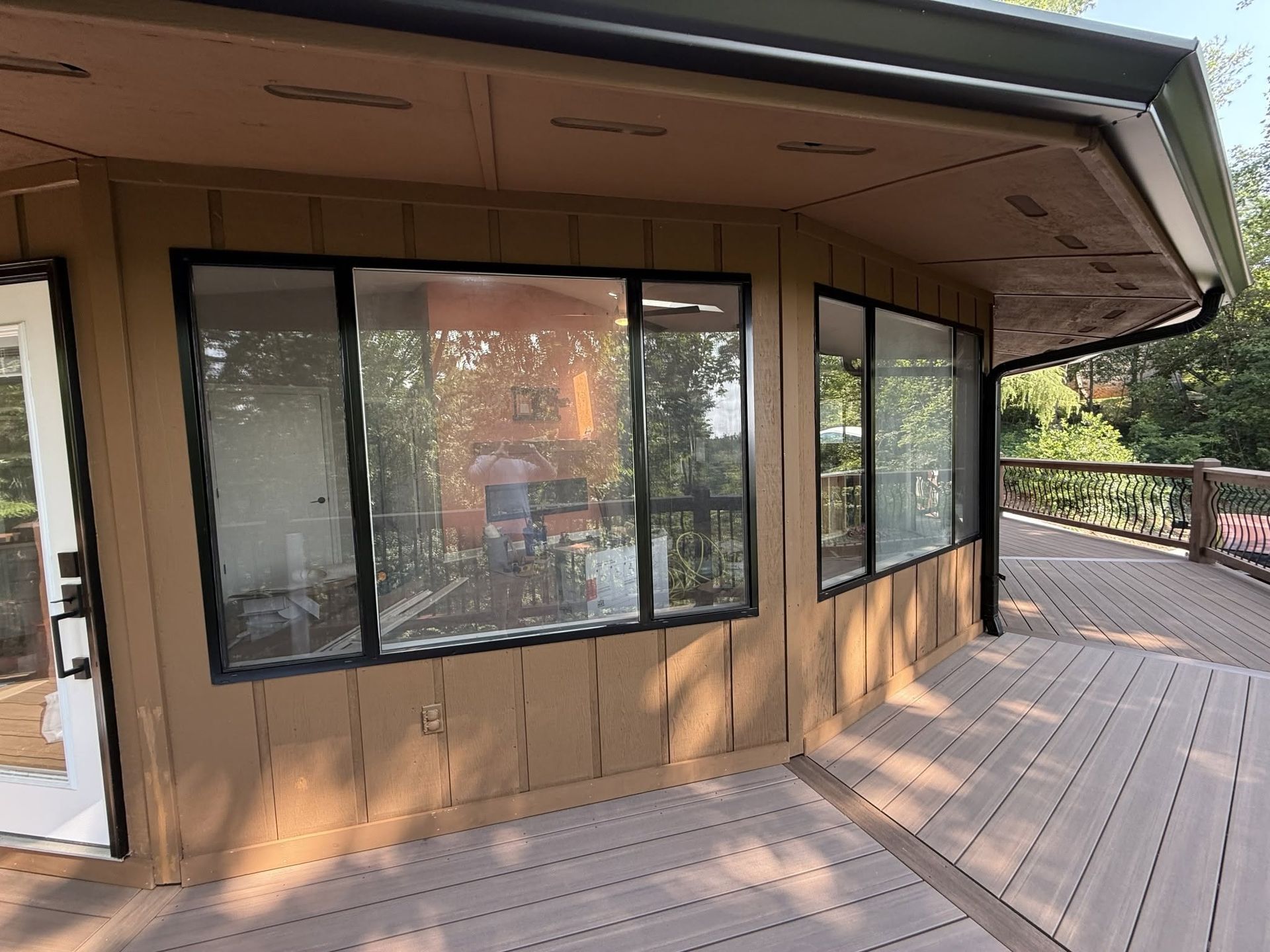 Exterior of a tan house with large windows and a wooden deck wrapping around the corner
