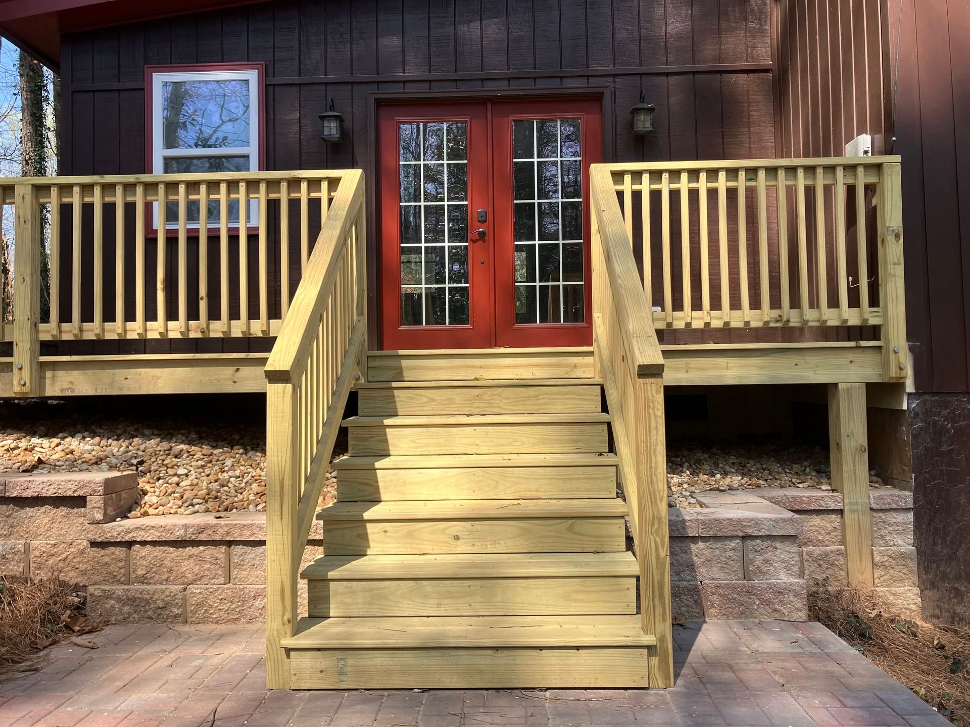 Wooden front porch with stairs, railings, and red double doors on a brown house.