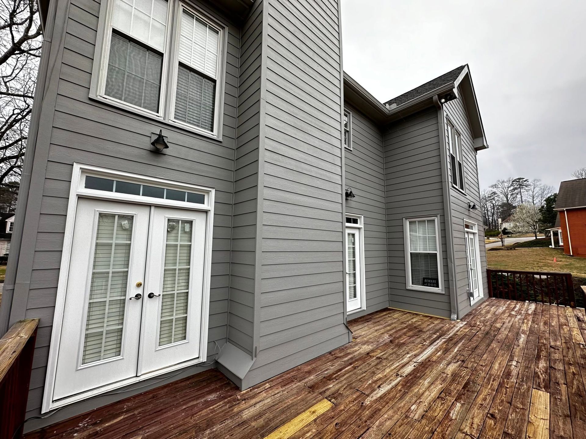 Gray two-story house with white trim and a wooden deck after rain