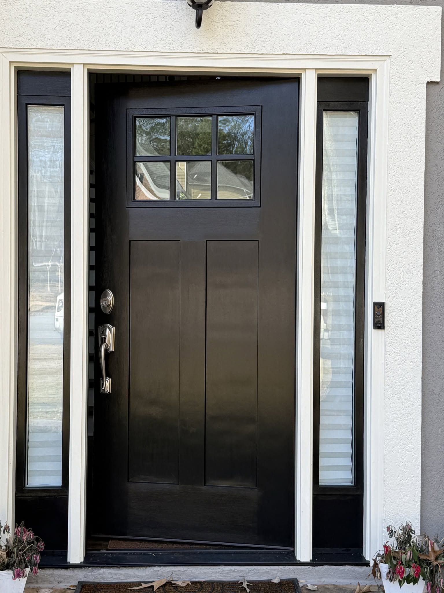 Black front door with narrow side windows and small upper window, set in a light stucco entryway