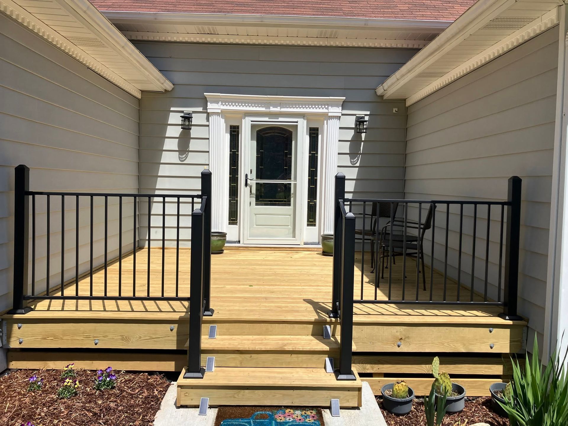 Front porch with black railings, wooden steps, and white French doors between gray house walls.