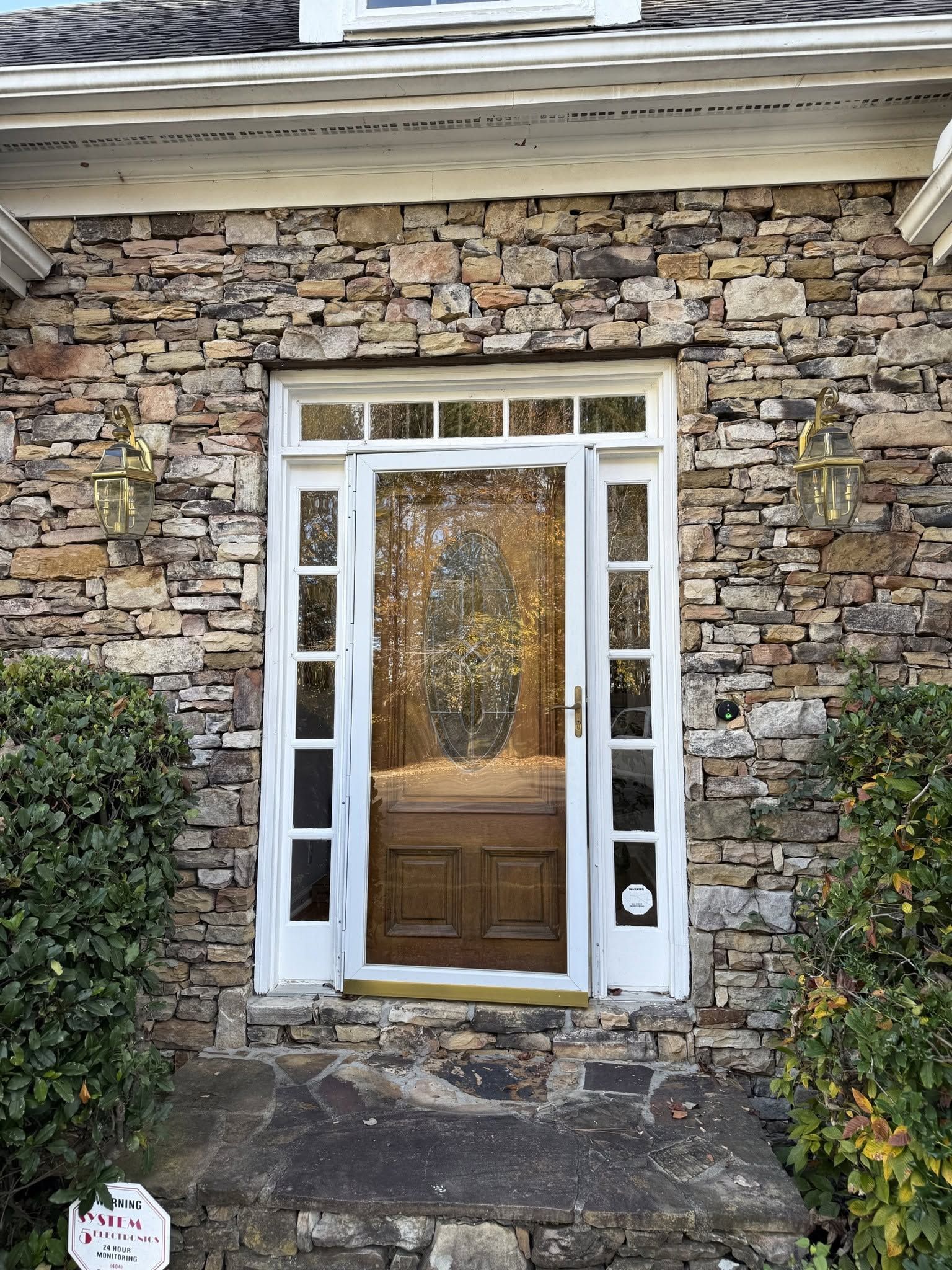 White-trimmed wooden front door in a stone house facade, framed by narrow windows and steps.