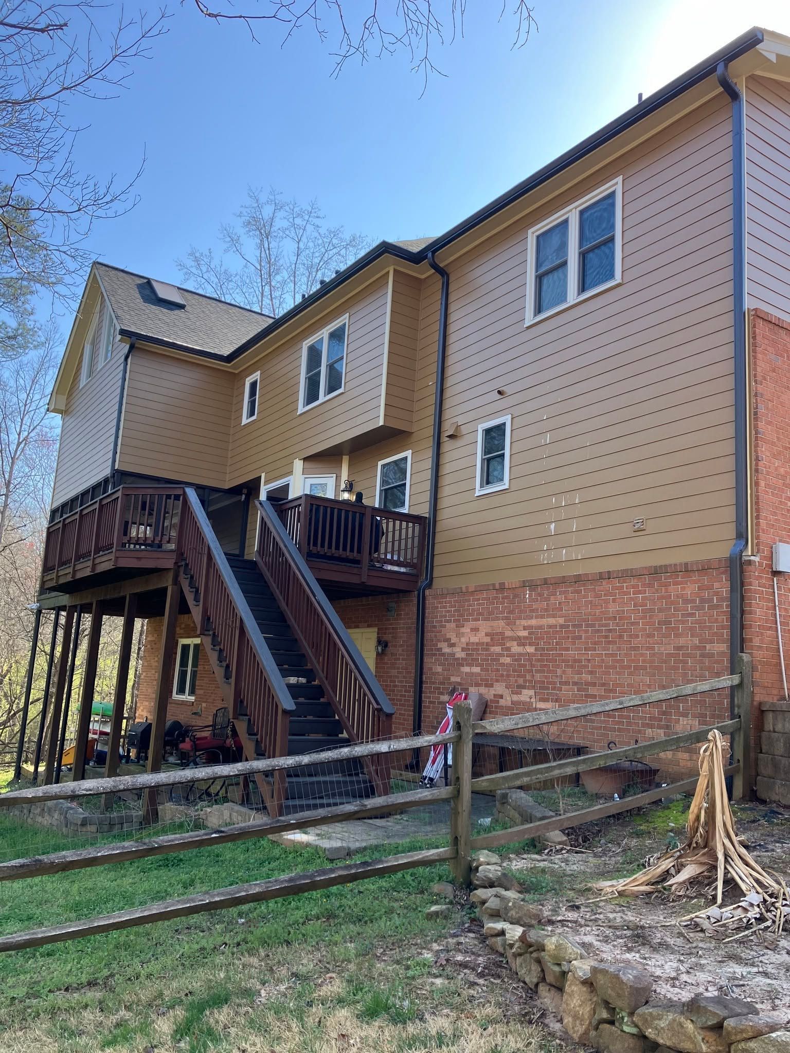 Two-story house with wood deck, exterior stairs, brick foundation, and yard after storm damage