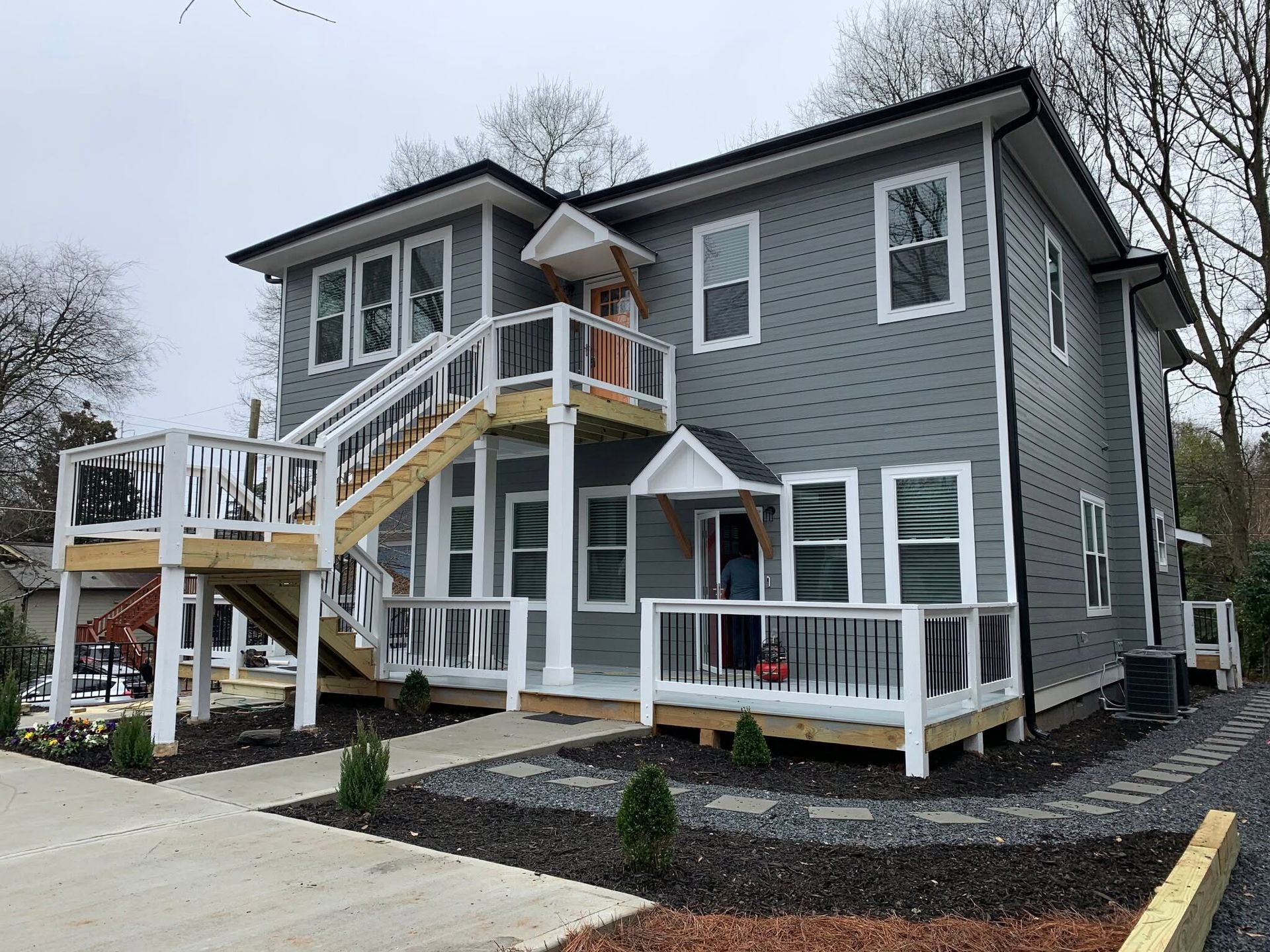 Gray two-story house with white trim, wheelchair ramp, and front porch deck in a snowy yard