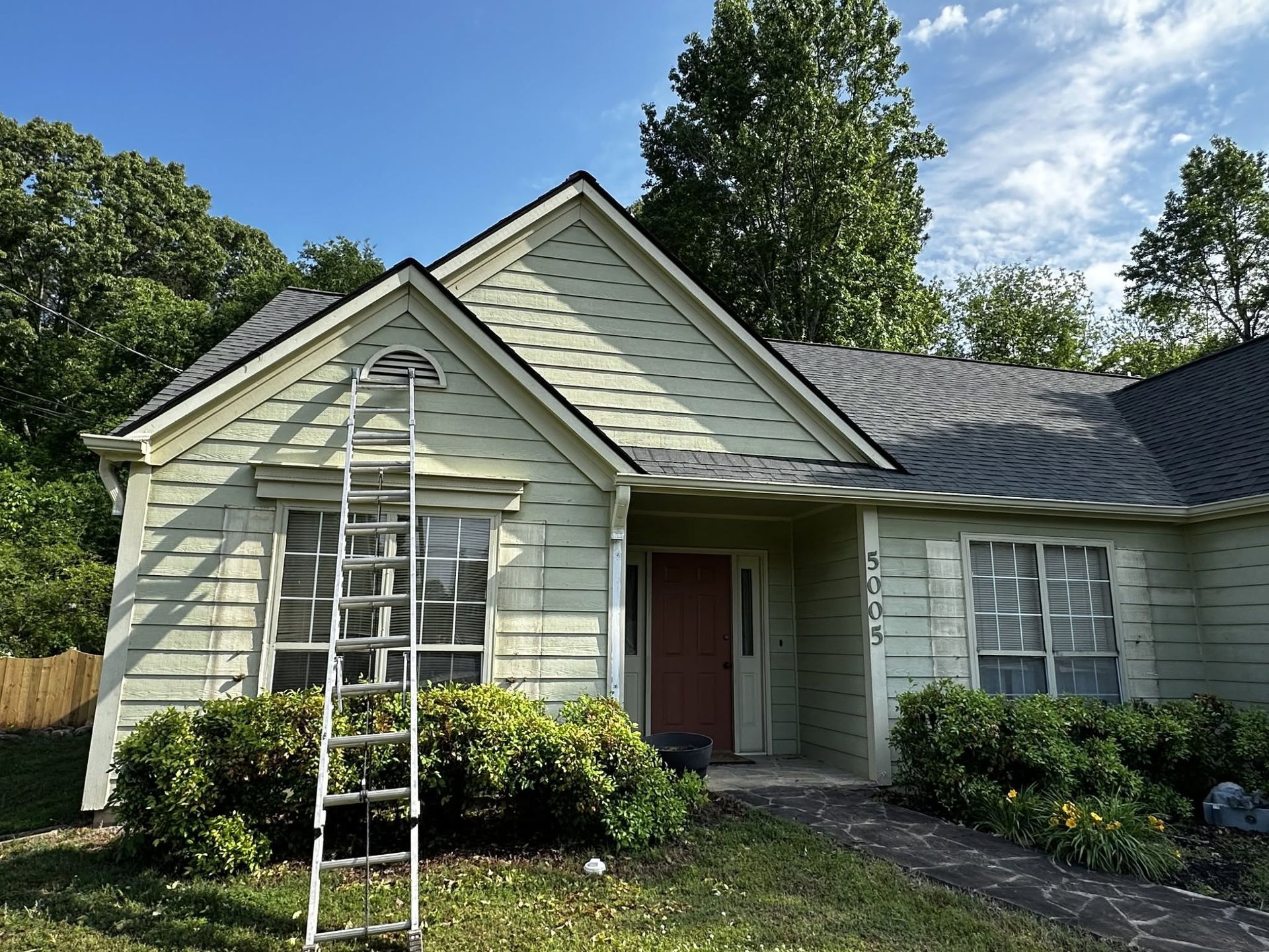 Single-story house with pale siding, front door, windows, and a ladder leaning against the facade.