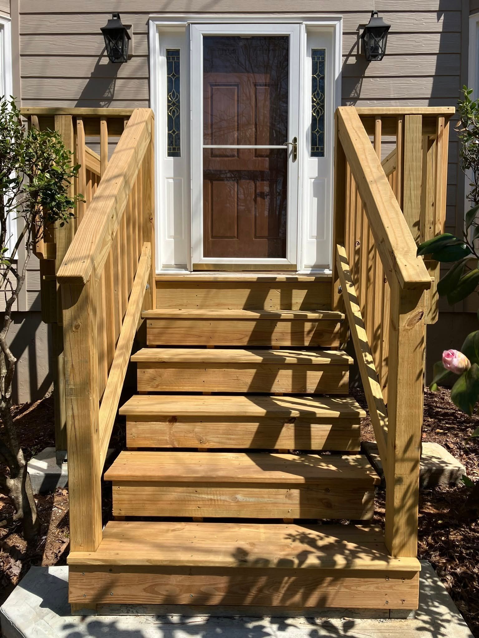 Wooden front stairs leading to a door, with railings and porch lights on a house exterior