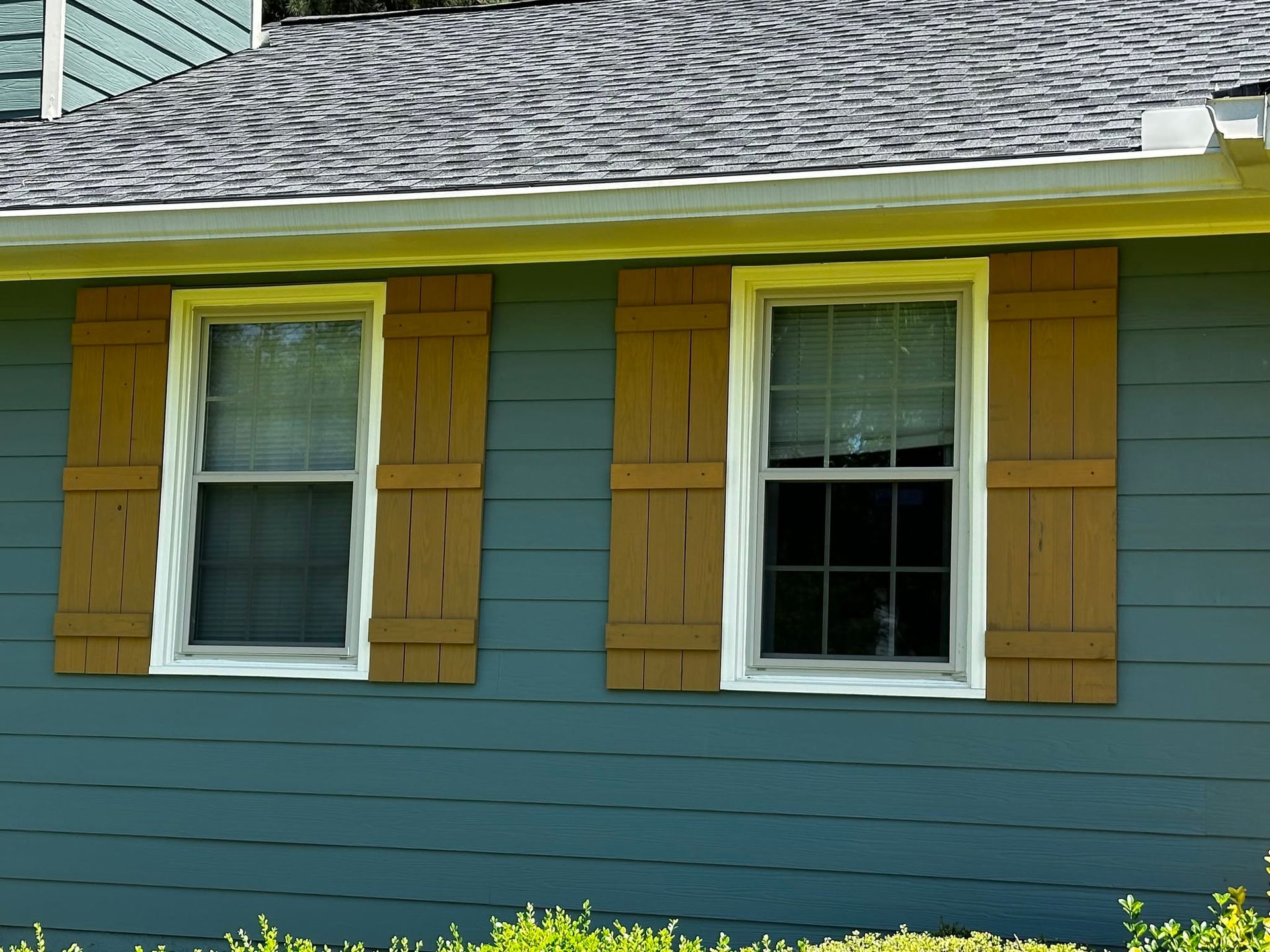 Two white-trimmed windows with yellow shutters on a blue house exterior under a gray shingled roof