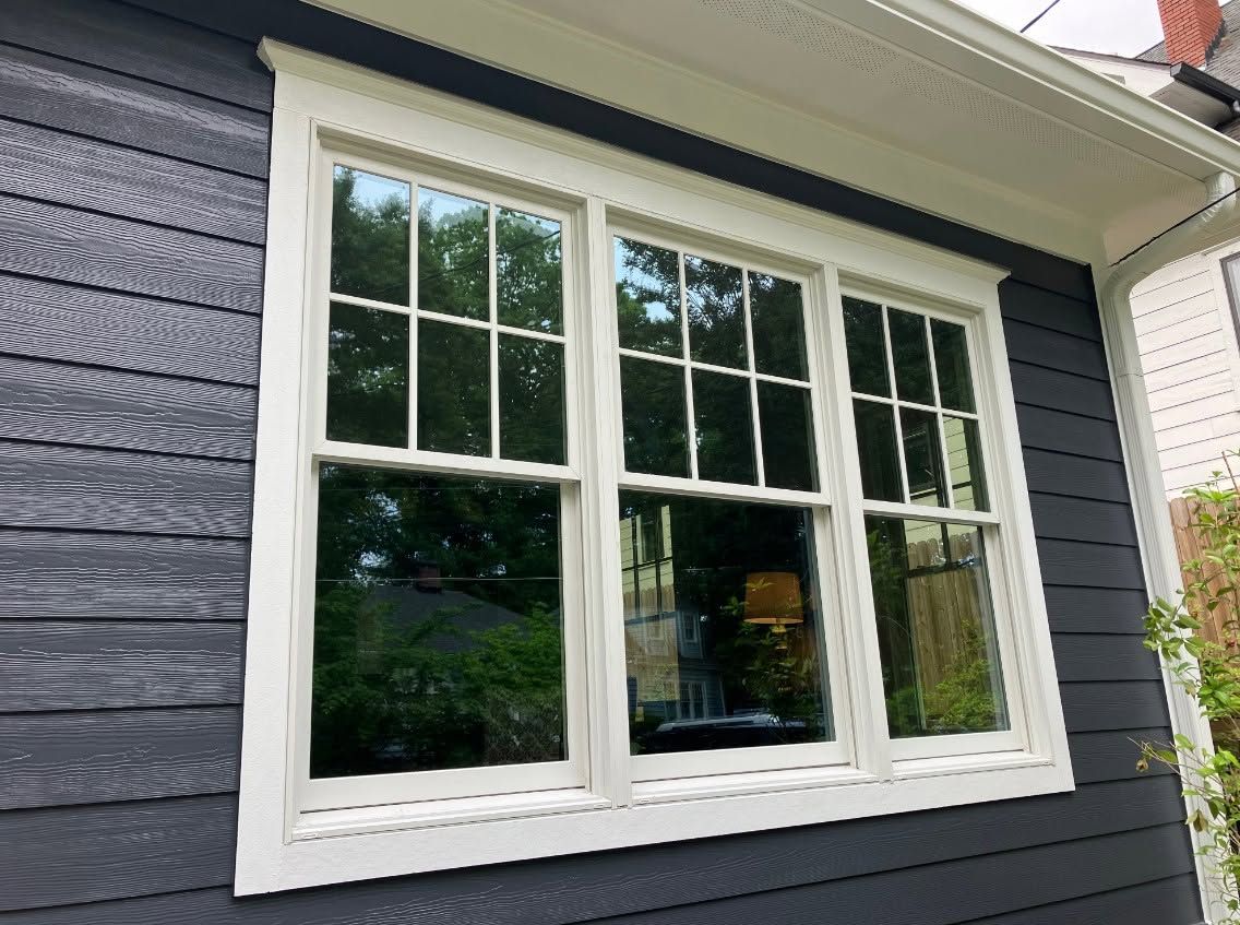 White-framed window on dark blue house siding with reflections of trees and sky