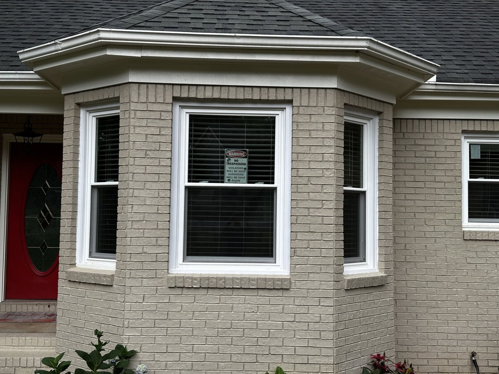 Front of a brick house with a bay window and red front door
