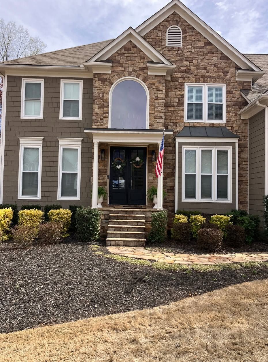 Two-story brick house with a front porch, steps, shutters, and an American flag by the door.