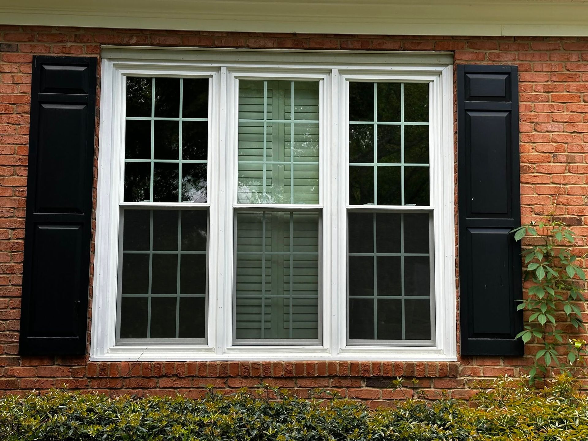 White-paned window with black shutters on a red brick wall