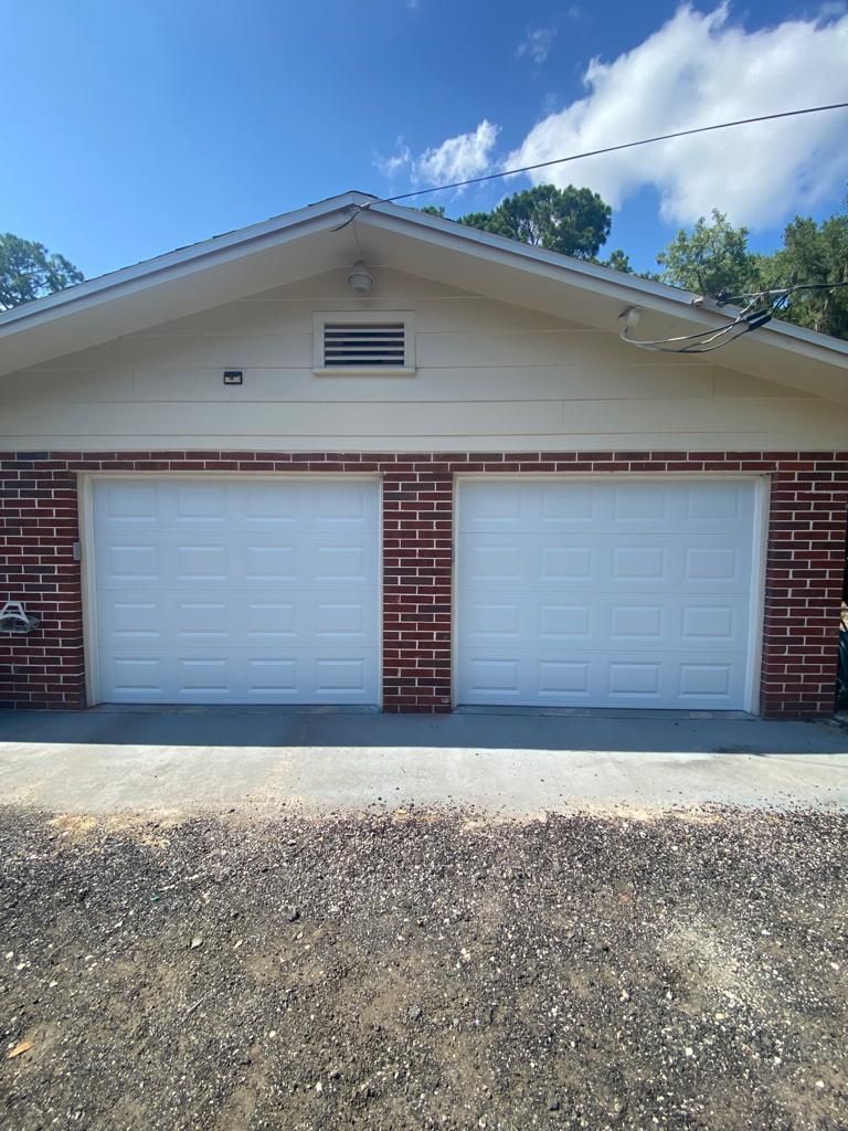 A house with two white garage doors and a brick wall.