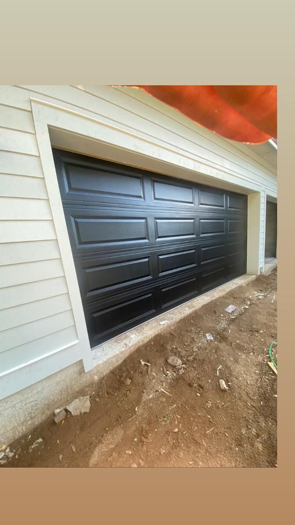 A black garage door is sitting on the side of a house.