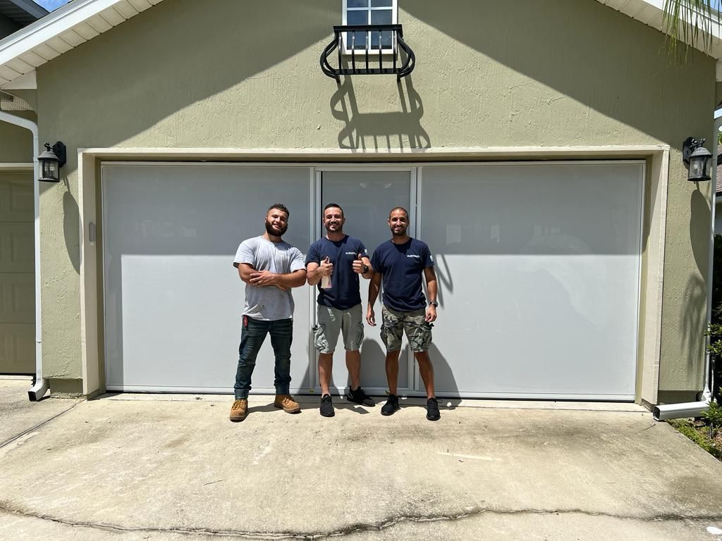 Three men are standing in front of a garage door.