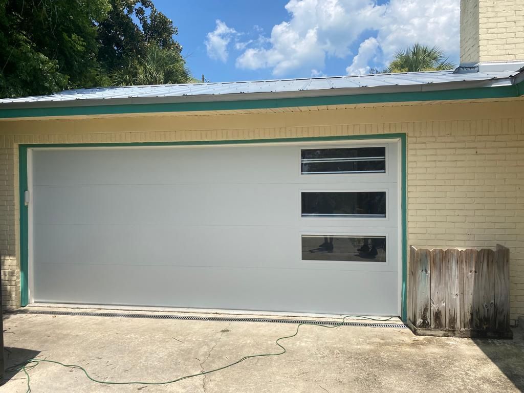 A white garage door with three windows on a brick house.
